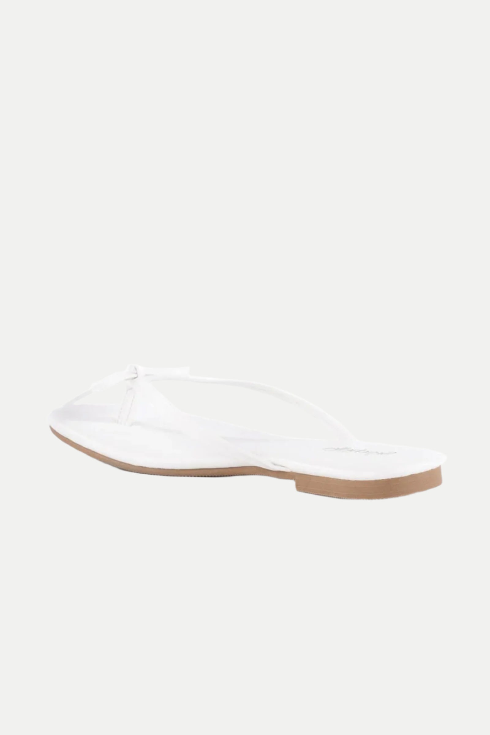 The Wish List Bow Thong Sandal is a white sandal with a flat, light brown sole, displayed on a plain white background and shown at an angle from the back and side.