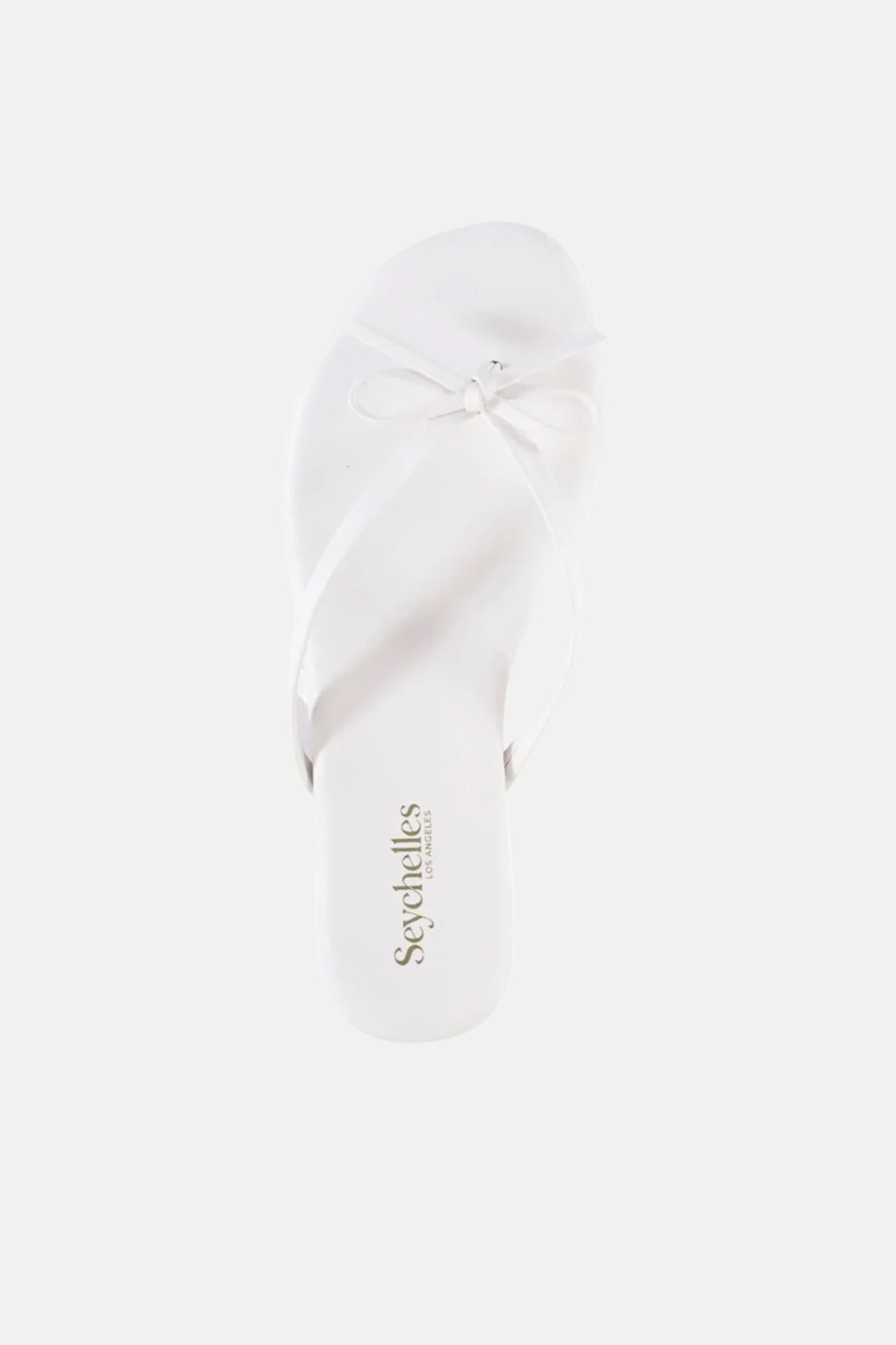 A single Wish List Bow Thong Sandal in white, featuring thin straps that cross at the toe and form a small bow, with Seychelles on the insole. The sandal is displayed against a plain white background.