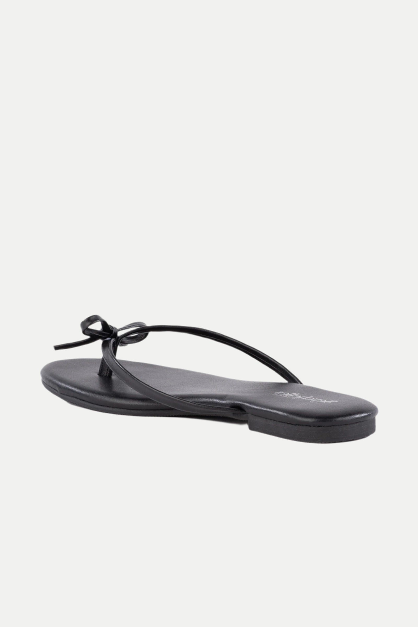 The Wish List Bow Thong Sandal is a black flat sandal featuring a thin strap and a small bow on top, shown from the back left against a white background.