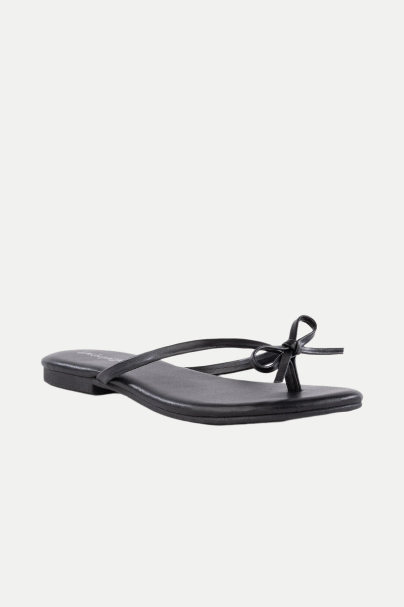 The Wish List Bow Thong Sandal is a black flat sandal featuring thin straps and a small bow on the front, shown against a white background.