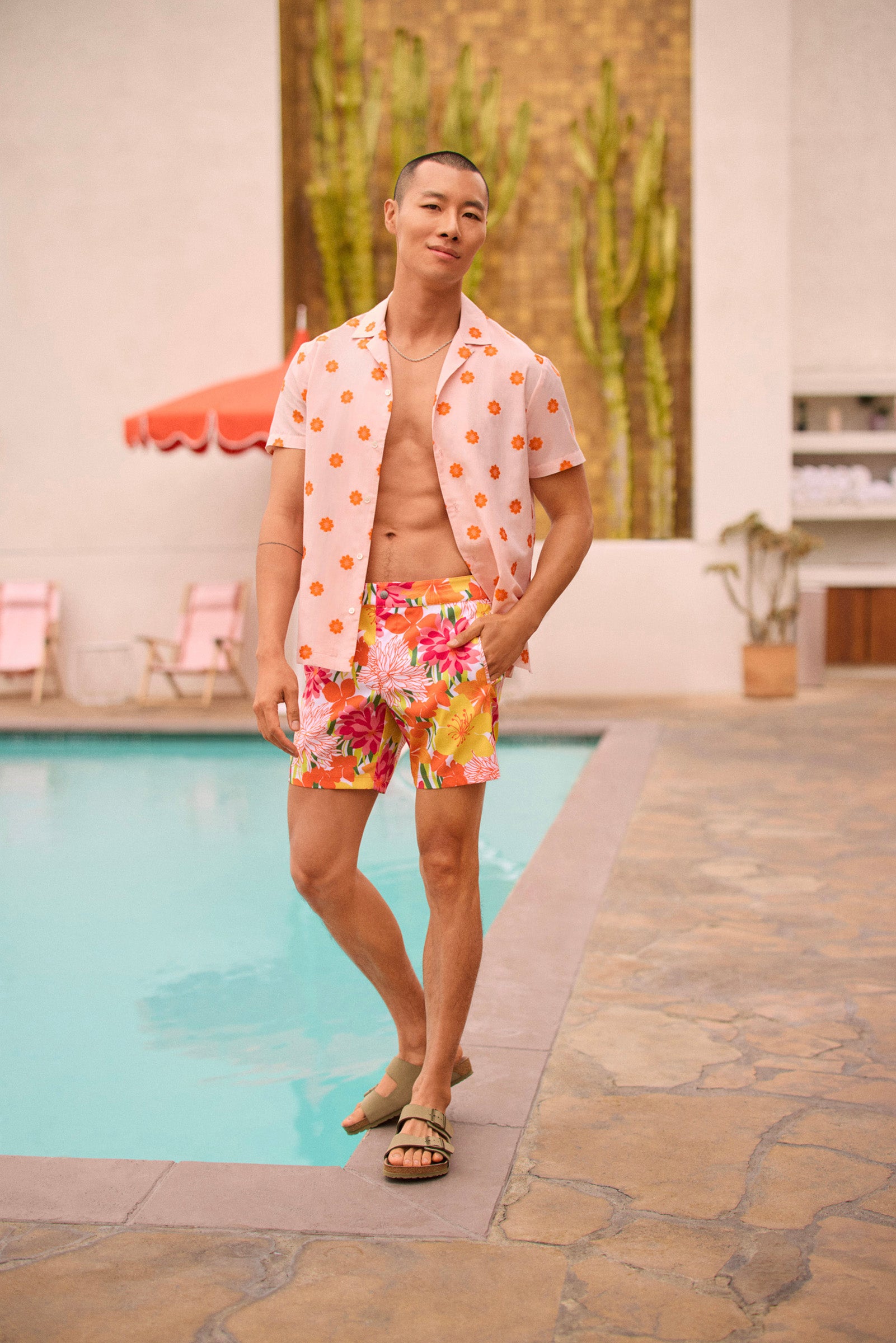 A man smiles by a pool, wearing the Felix Camp Shirt - Daisy Dots. Cacti and pink chairs are visible in the background.