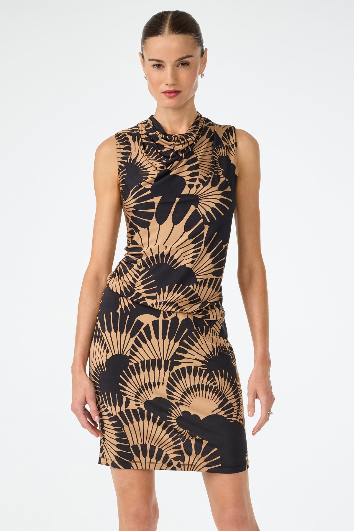 A woman stands against a plain white background wearing the Lenaya 3 Drape Dress in Juniper Jersey, a sleeveless, fitted style featuring a bold black and tan abstract leaf print. Her hair is slicked back and she looks forward with a neutral expression.