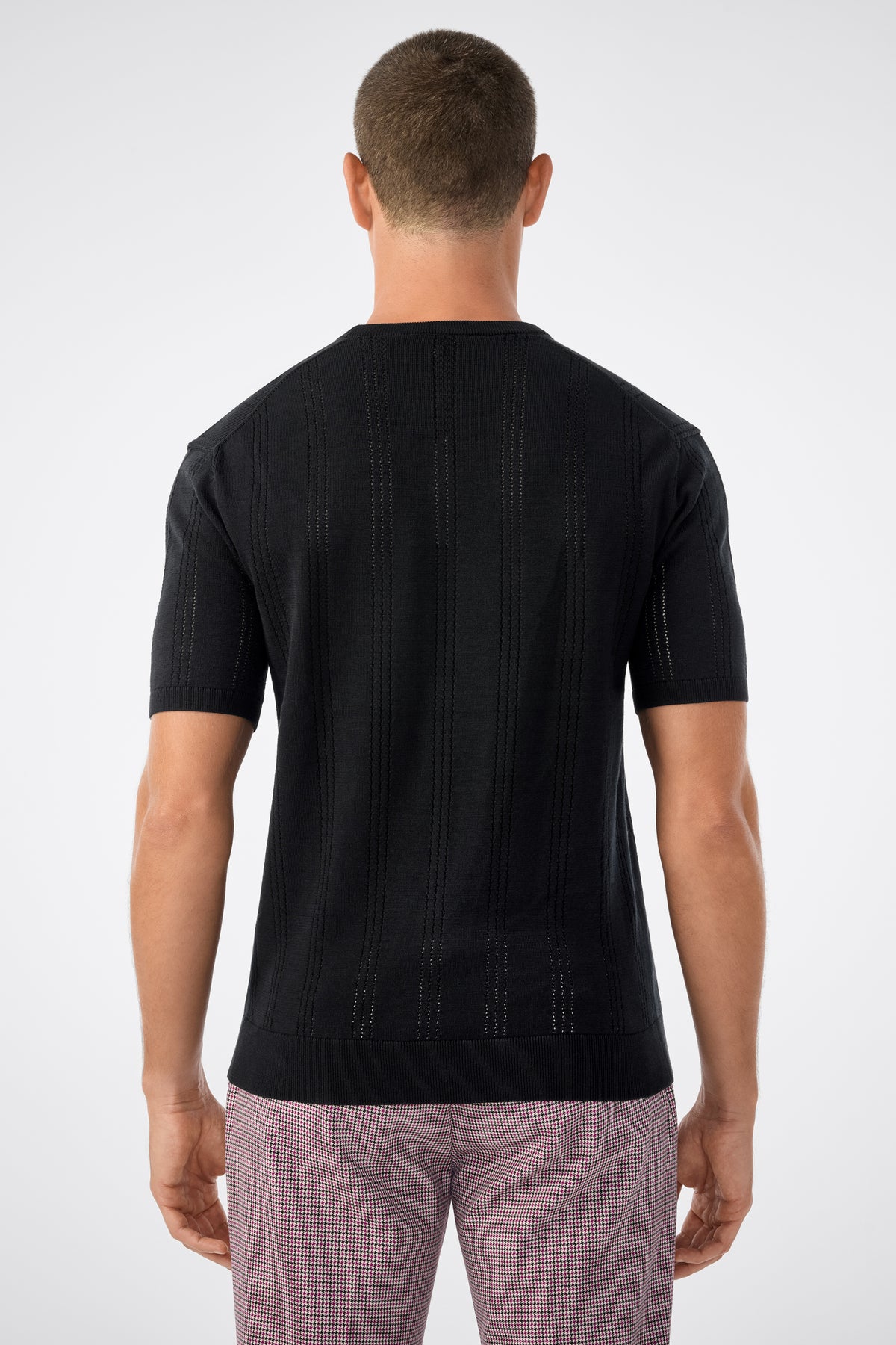 A man with short hair is shown from behind, wearing the Carlo Ss Crewneck in black and light pink checkered pants against a plain light gray background.