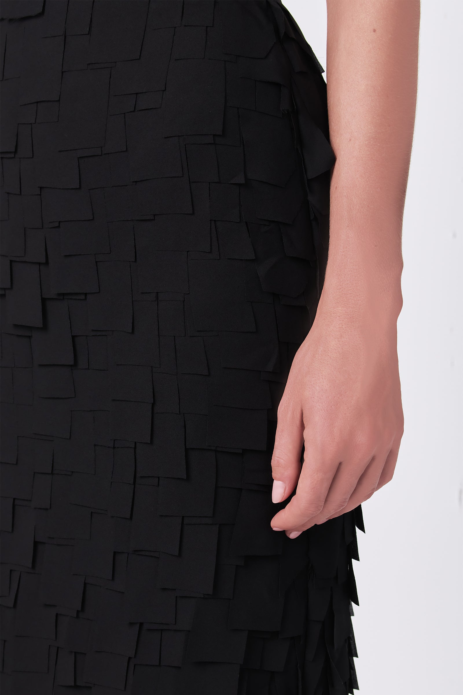 A close-up of a hand resting on the Dita Midi Pencil Skirt - Flutter Chiffon, featuring a textured, layered pattern of small, overlapping chiffon squares.