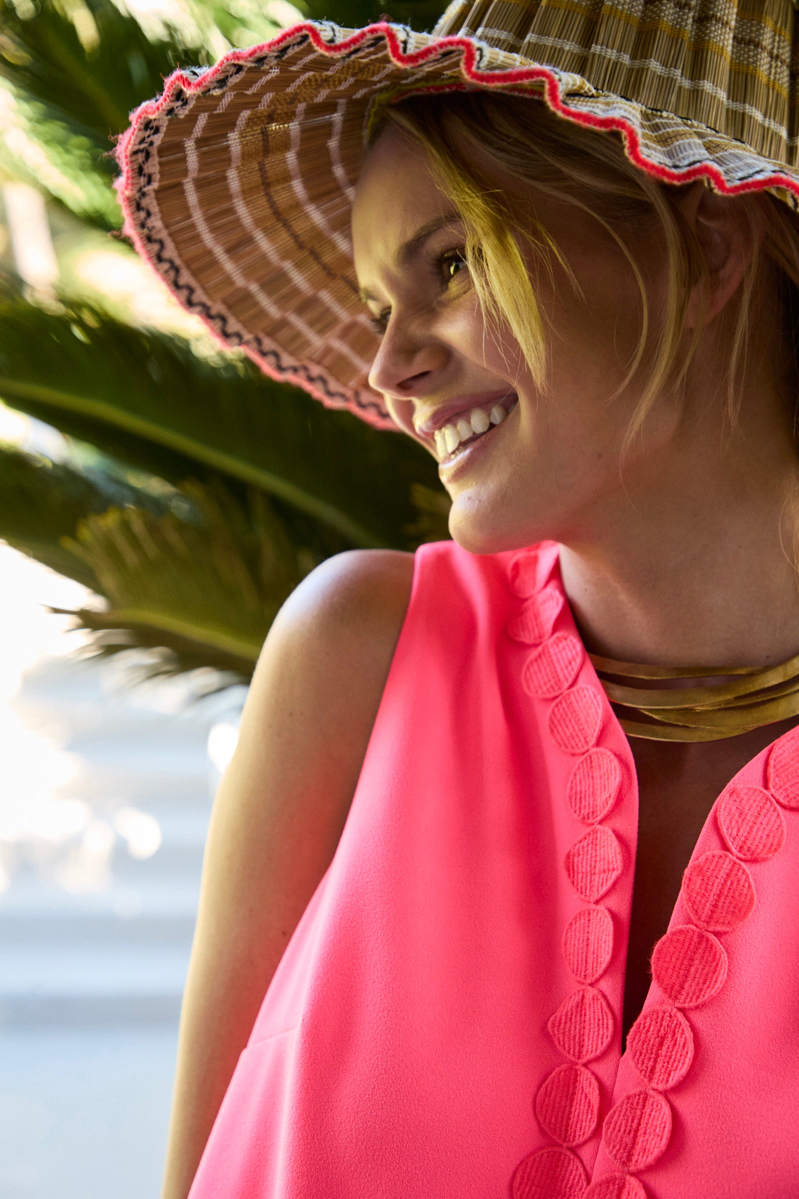 A woman wearing the Pavia Mini Dress and a wide-brimmed straw hat smiles while standing outdoors in sunlight.