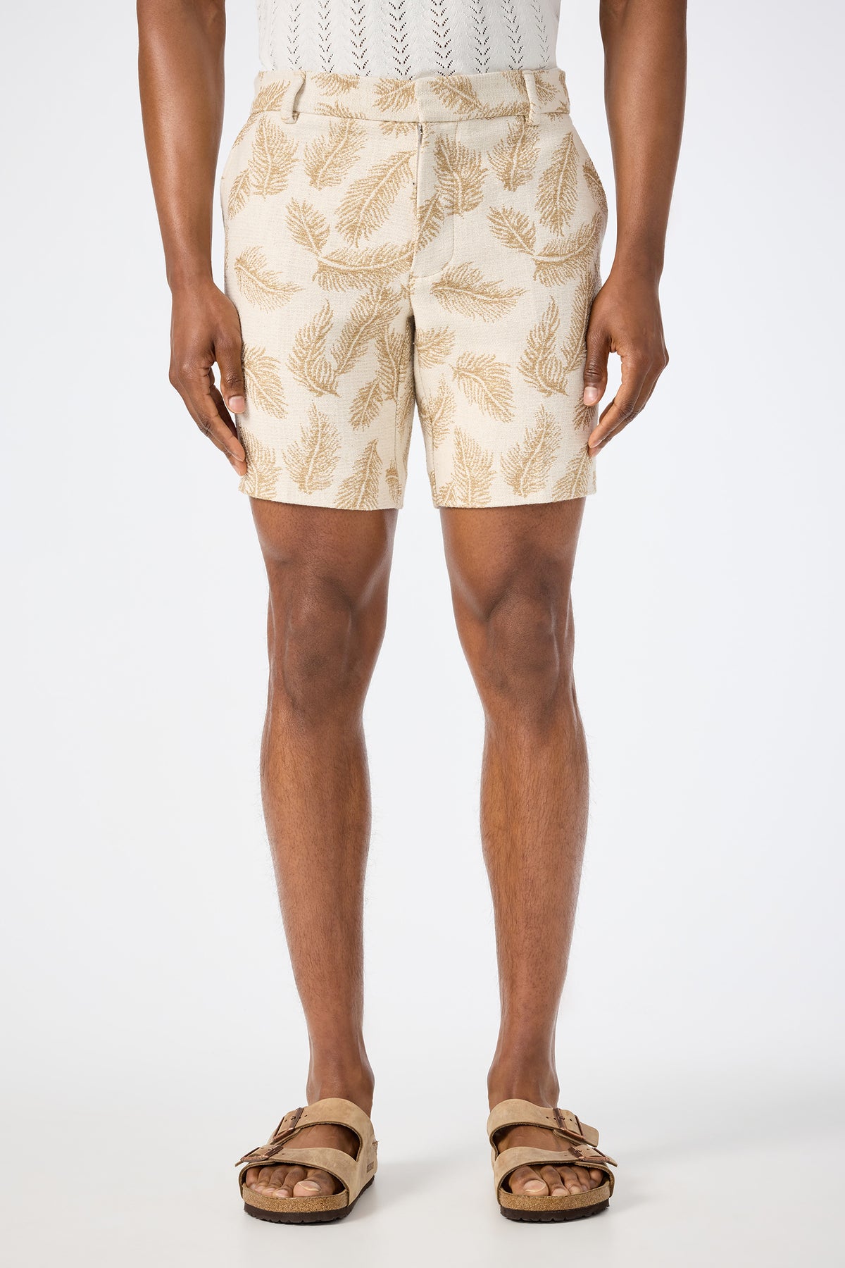 A person models the Lawrence Short in Desert Fronds Jacquard, paired with a white knit top and tan sandals, standing against a plain white background with only the lower body visible.