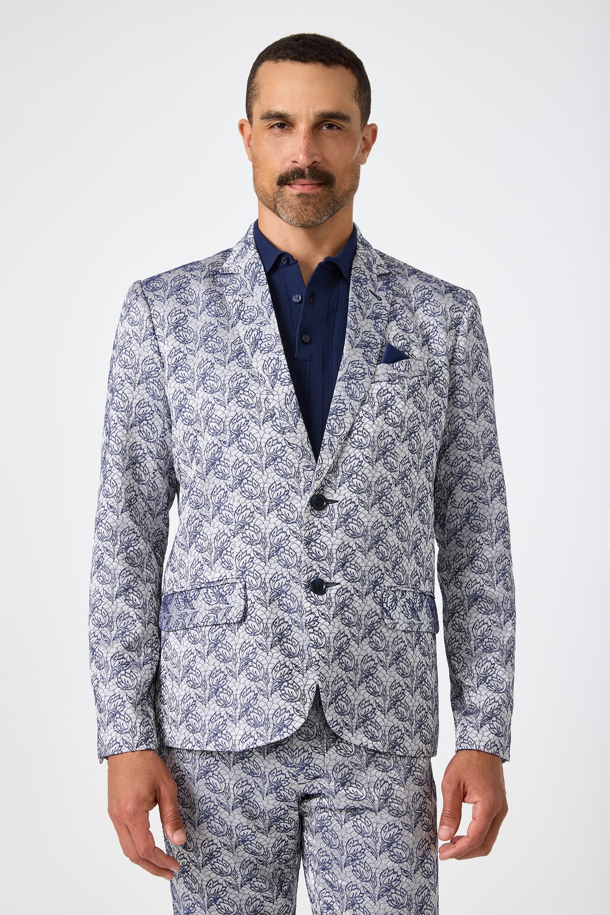 A man with short hair and a mustache wears the Thurston Blazer in Efflorescent Jacquard with a dark blue shirt, standing against a plain light background.
