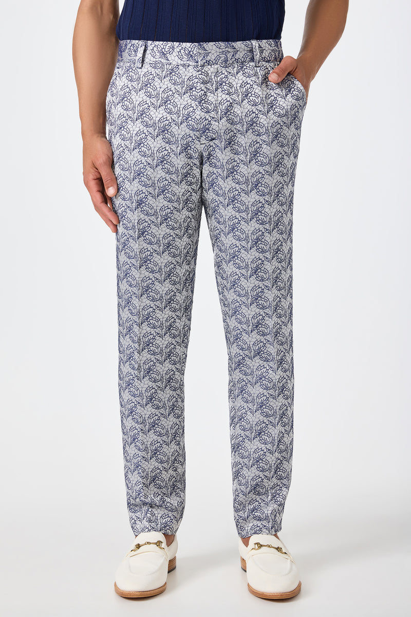 A person wearing Clyde Slim Trouser in Efflorescent Jacquard, styled with a navy shirt and white tassel loafers, stands against a light background.