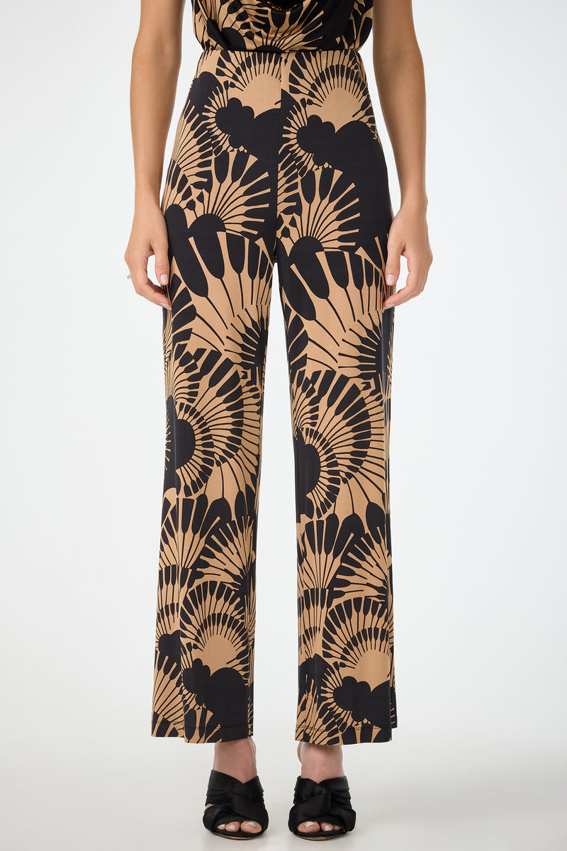 Someone wears Atoll Wide-Leg Cropped Pants in Juniper Jersey featuring a bold black and tan abstract fan pattern, paired with black open-toe heels, standing against a plain white background.