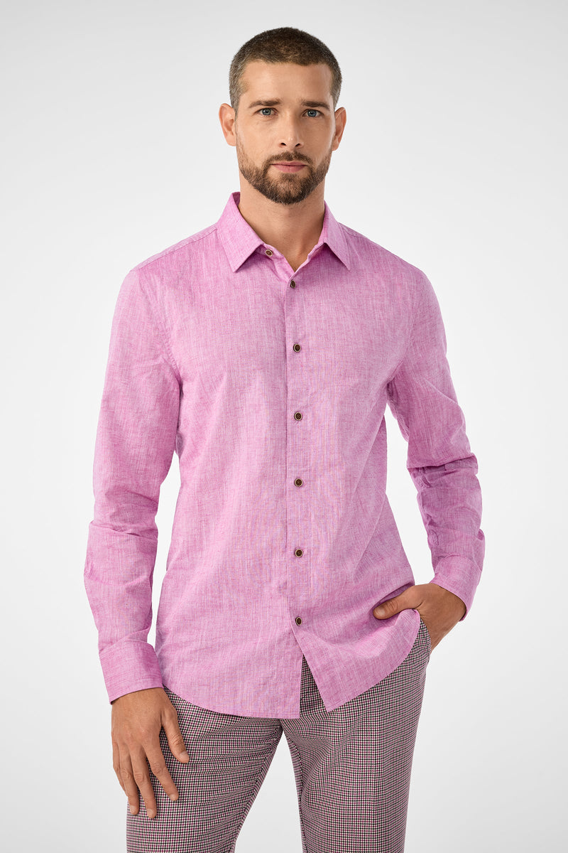 A man with short hair and a beard wears the Aaron Slim Fit Long-Sleeve Shirt in Geranium and checkered pants, standing confidently with one hand in his pocket against a plain, light background.