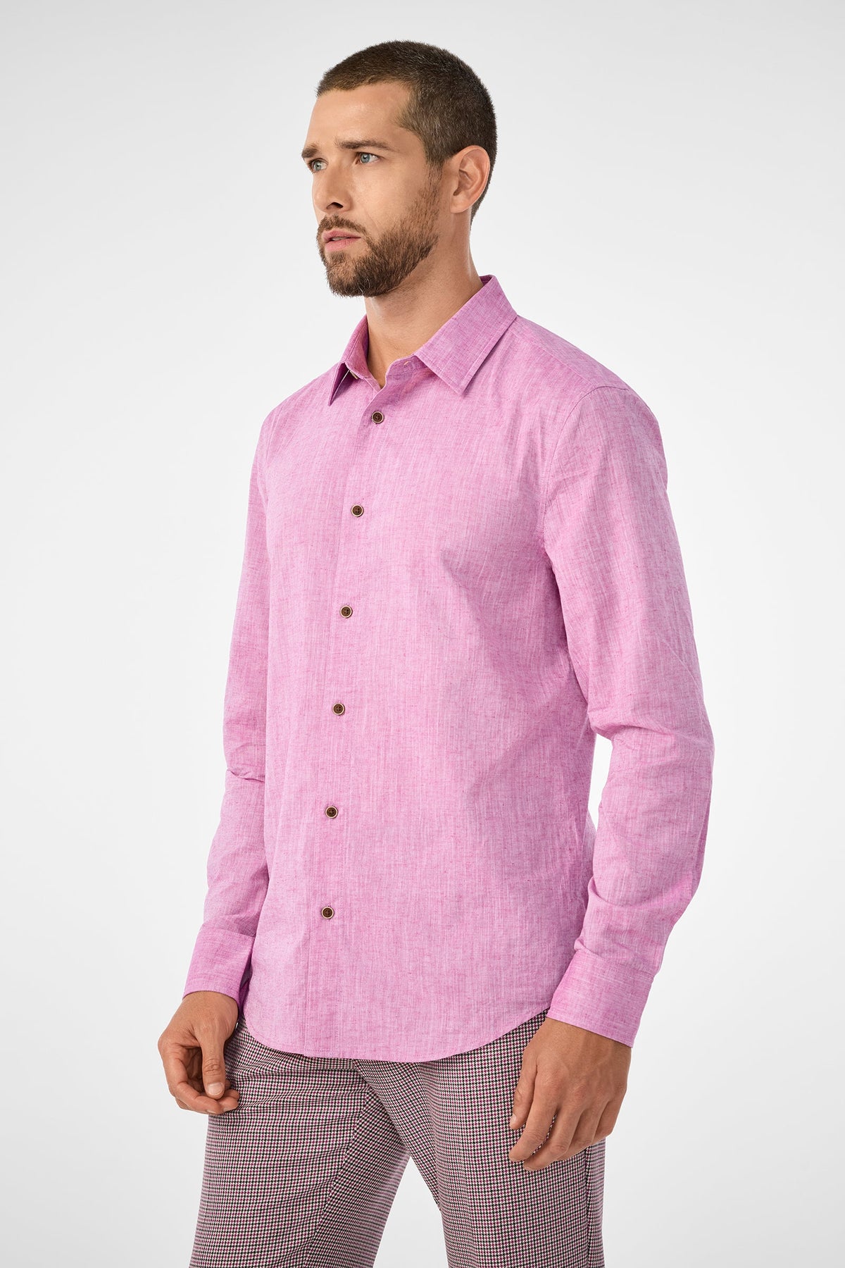 A man with short hair and a beard wears the Aaron Slim Fit Long-Sleeve Shirt in Geranium, paired with patterned pants, standing against a plain light background.