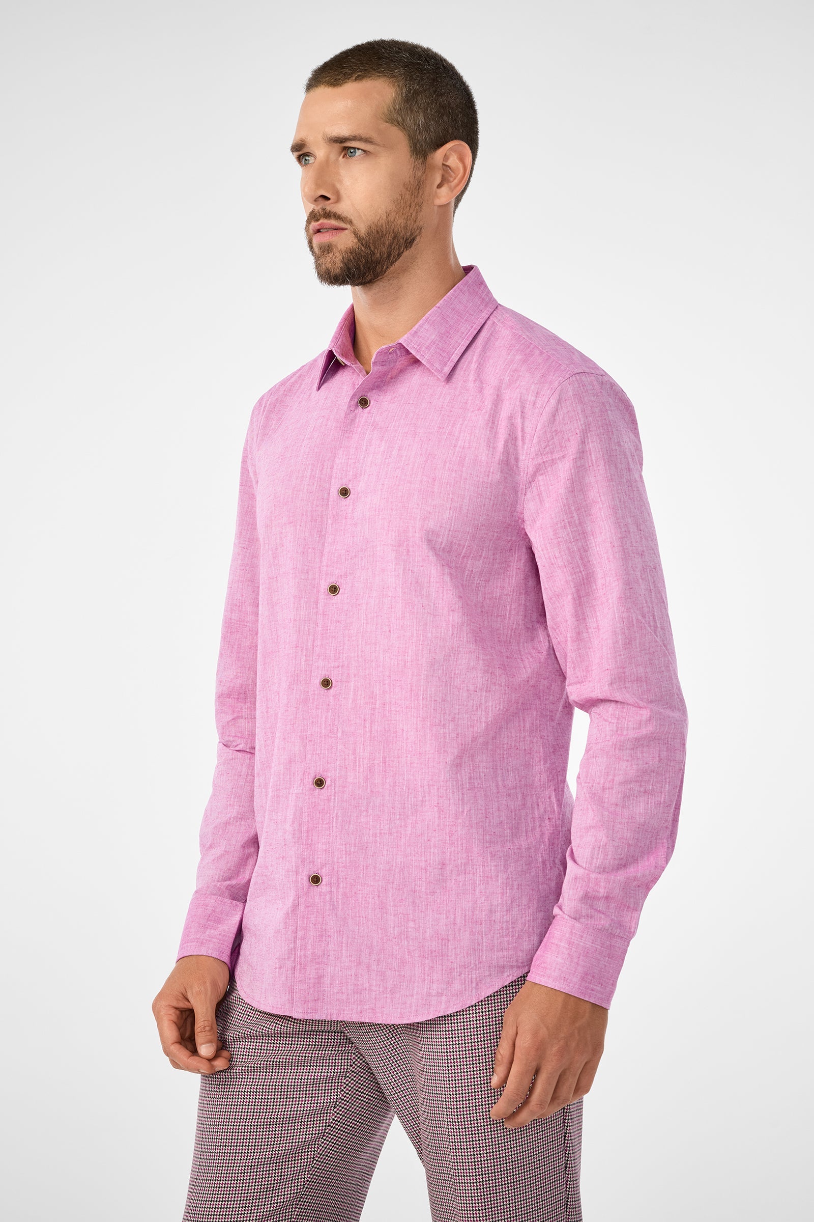 A man with short hair and a beard wears the Aaron Slim Fit Long-Sleeve Shirt in Geranium, paired with patterned pants, standing against a plain light background.