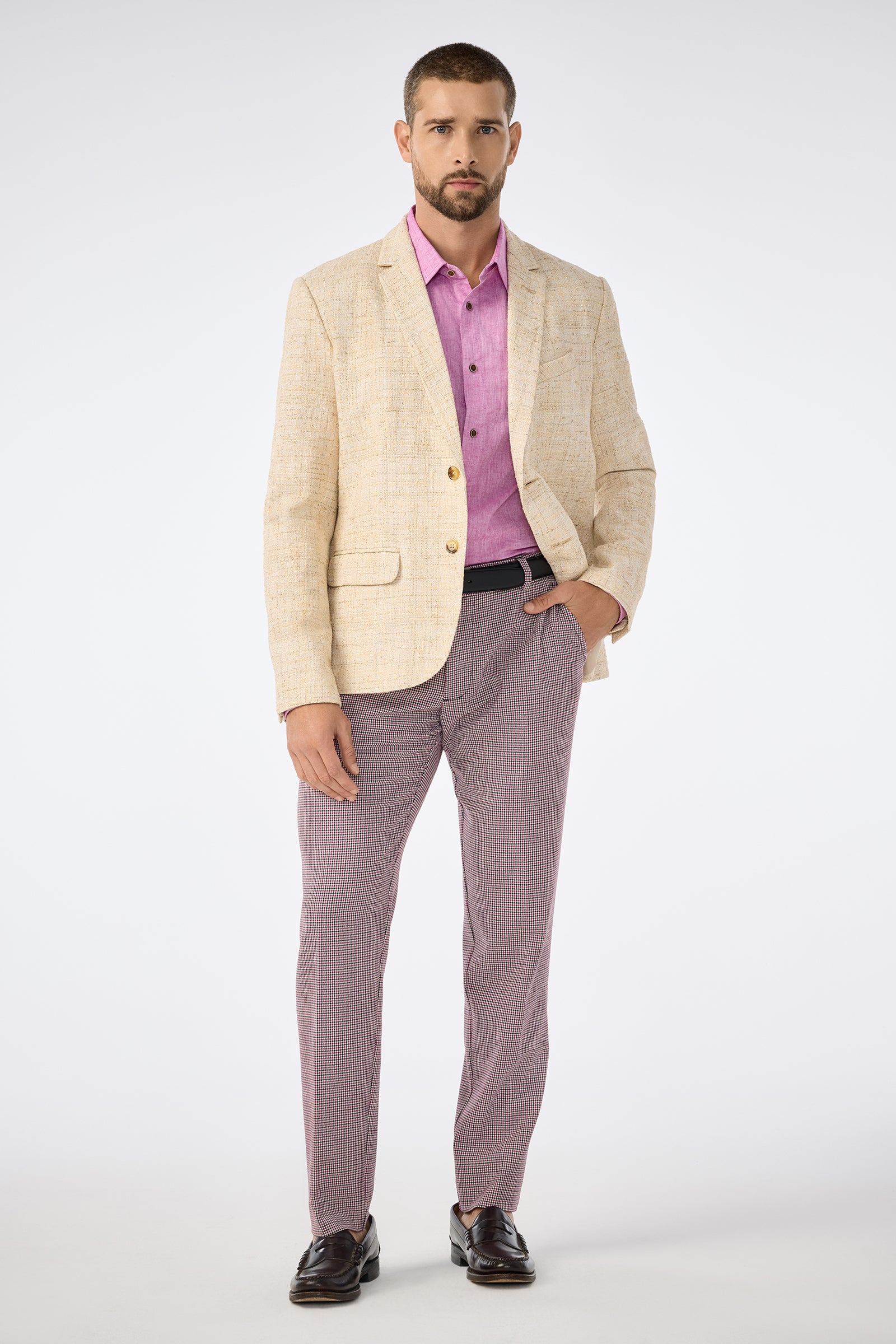 A man with short hair and a beard, wearing the Thurston Blazer over a pink shirt, plaid trousers, black belt, and dark loafers, stands against a plain background with a neutral expression.
