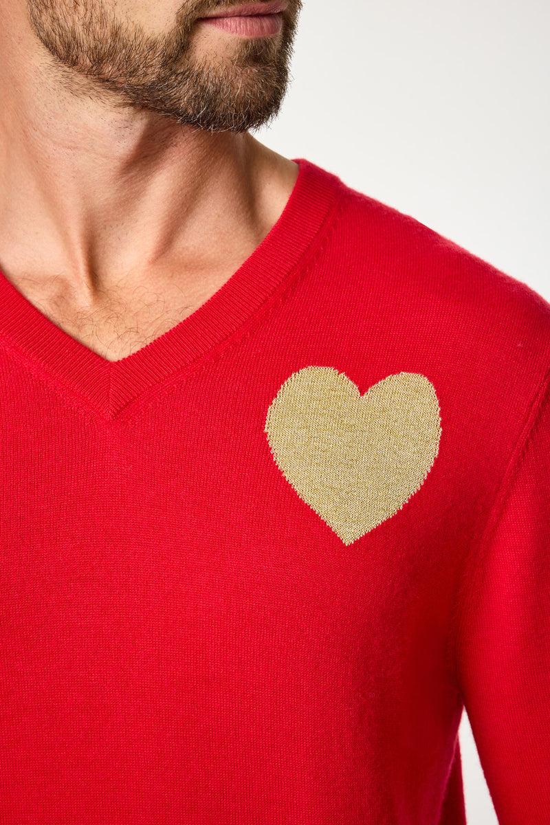 Someone wearing the Lover V-Neck Sweater, a bright red sweater with a large gold heart design on the left chest. Only the lower part of their face and neck are shown.