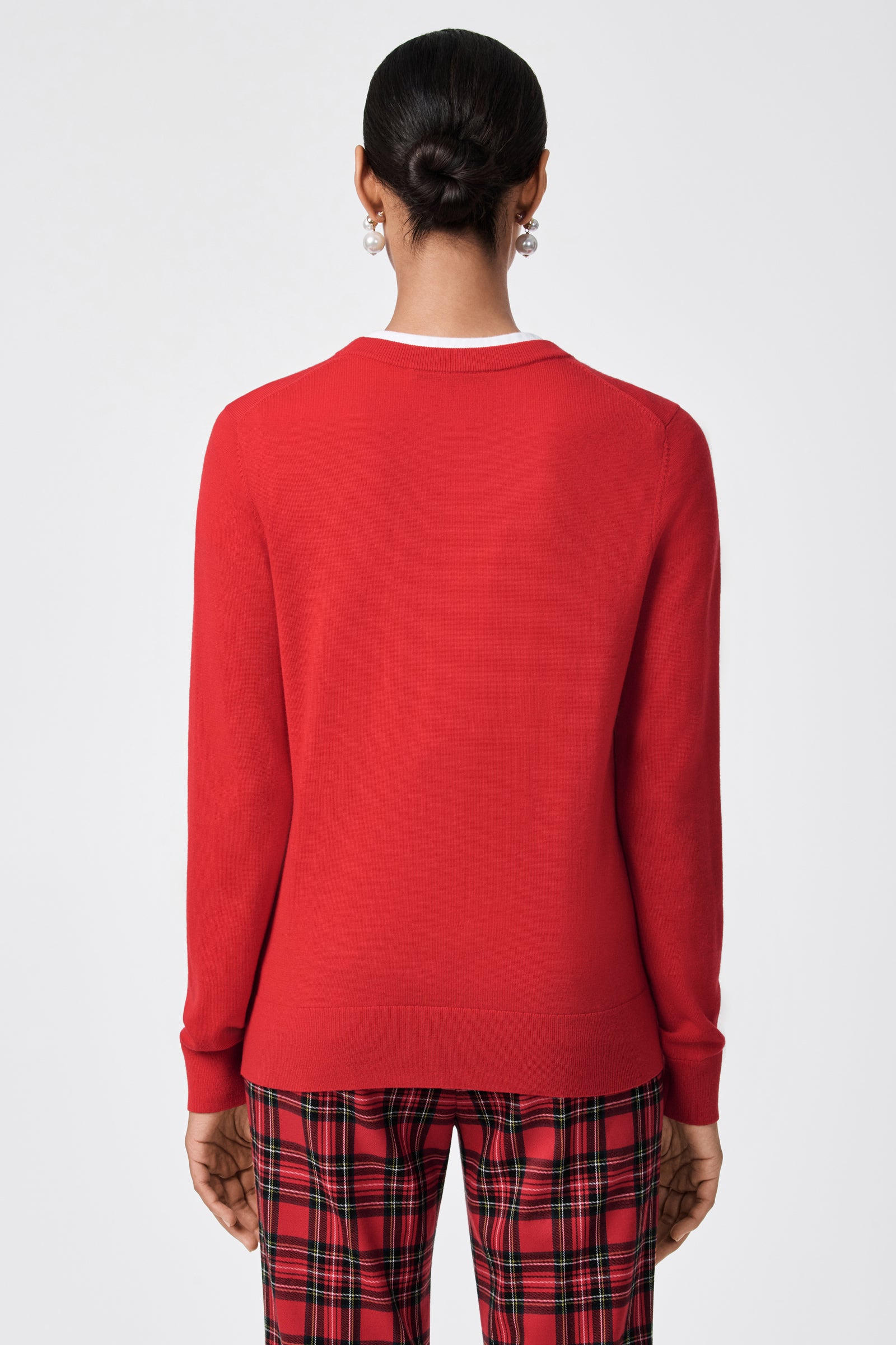 A person with dark hair in a low bun is shown from the back, wearing the Jaguar Heart Crewneck Sweater and red plaid pants against a plain light background.