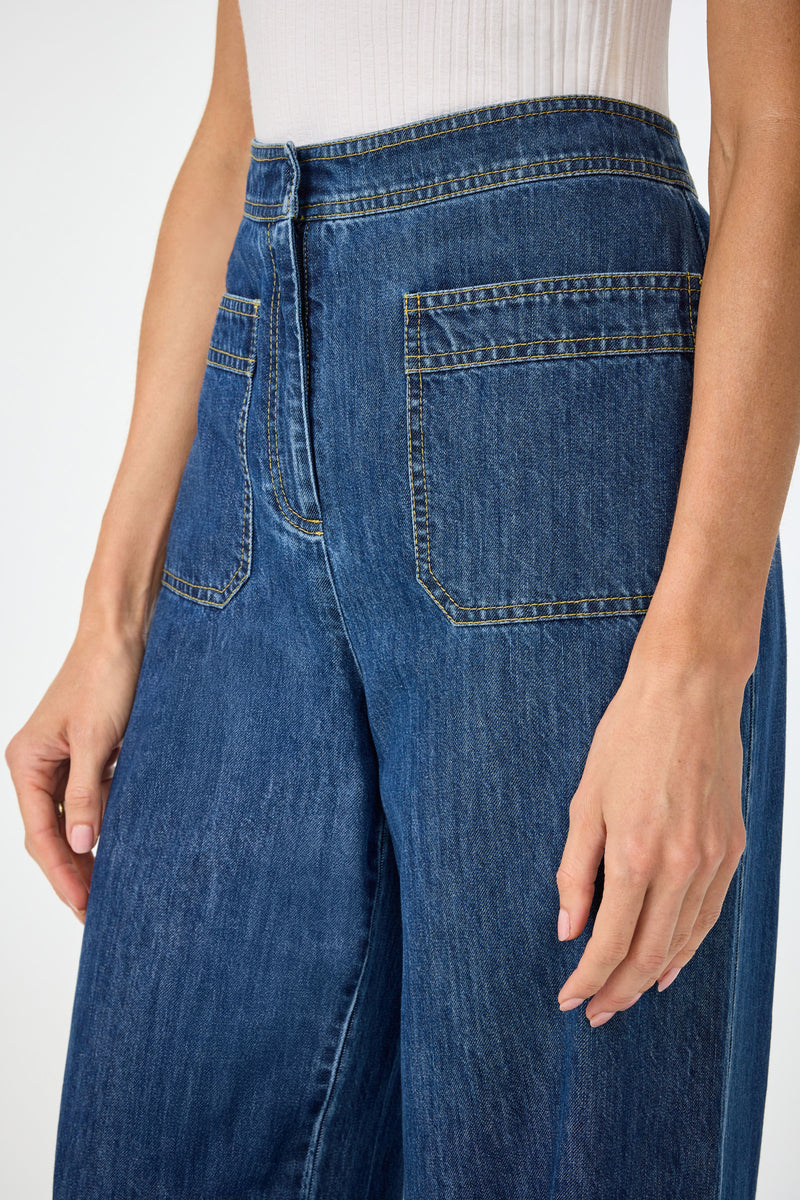 Wearing Ferrer Wide Leg Jean in high-waisted blue denim with large front pockets and visible stitching, paired with a white ribbed sleeveless top. Shown from the waist down.