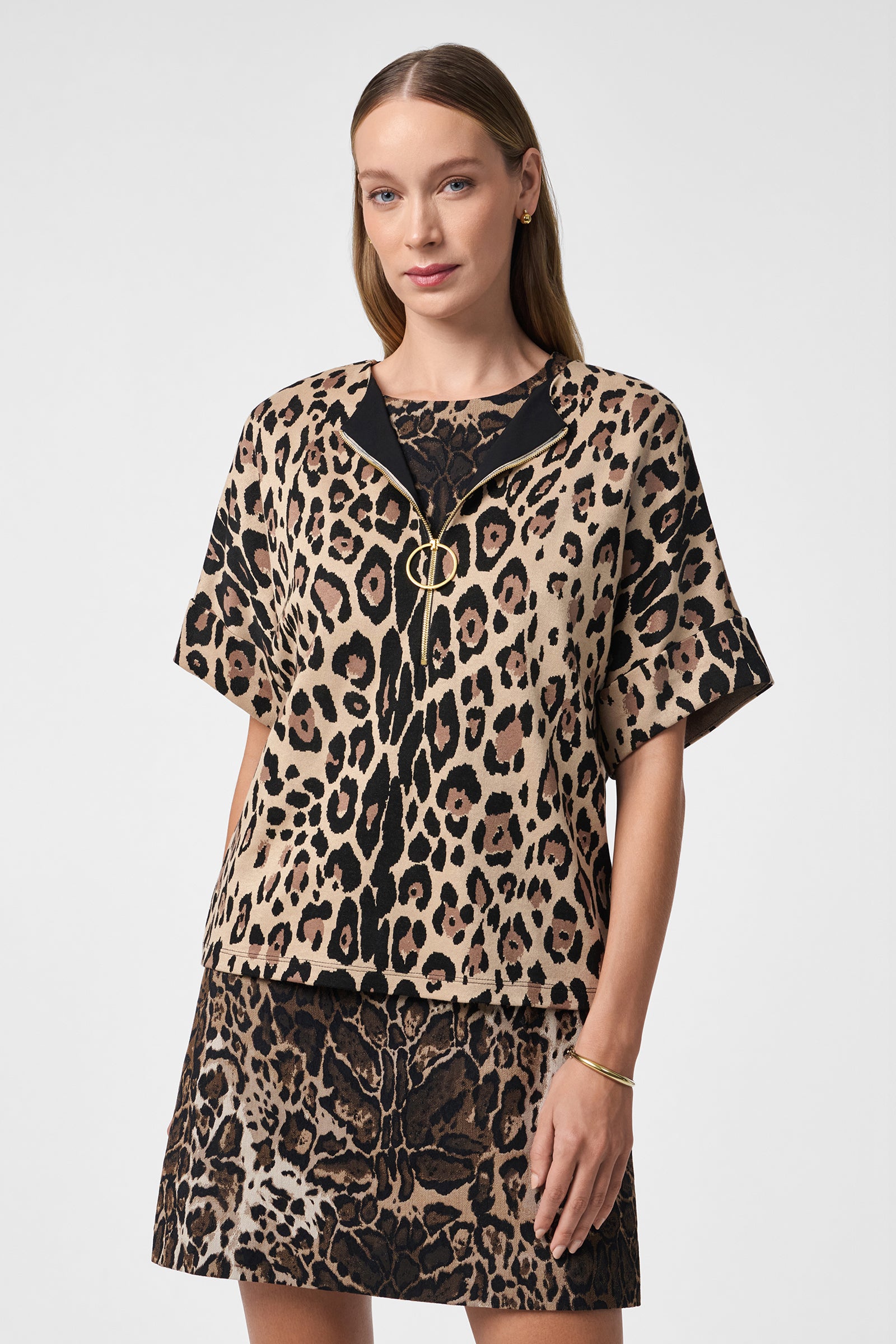 A woman with straight, light brown hair wears the Stagehands Top—a short-sleeved, leopard print blouse—paired with a matching skirt and gold jewelry, posing against a plain light gray background.