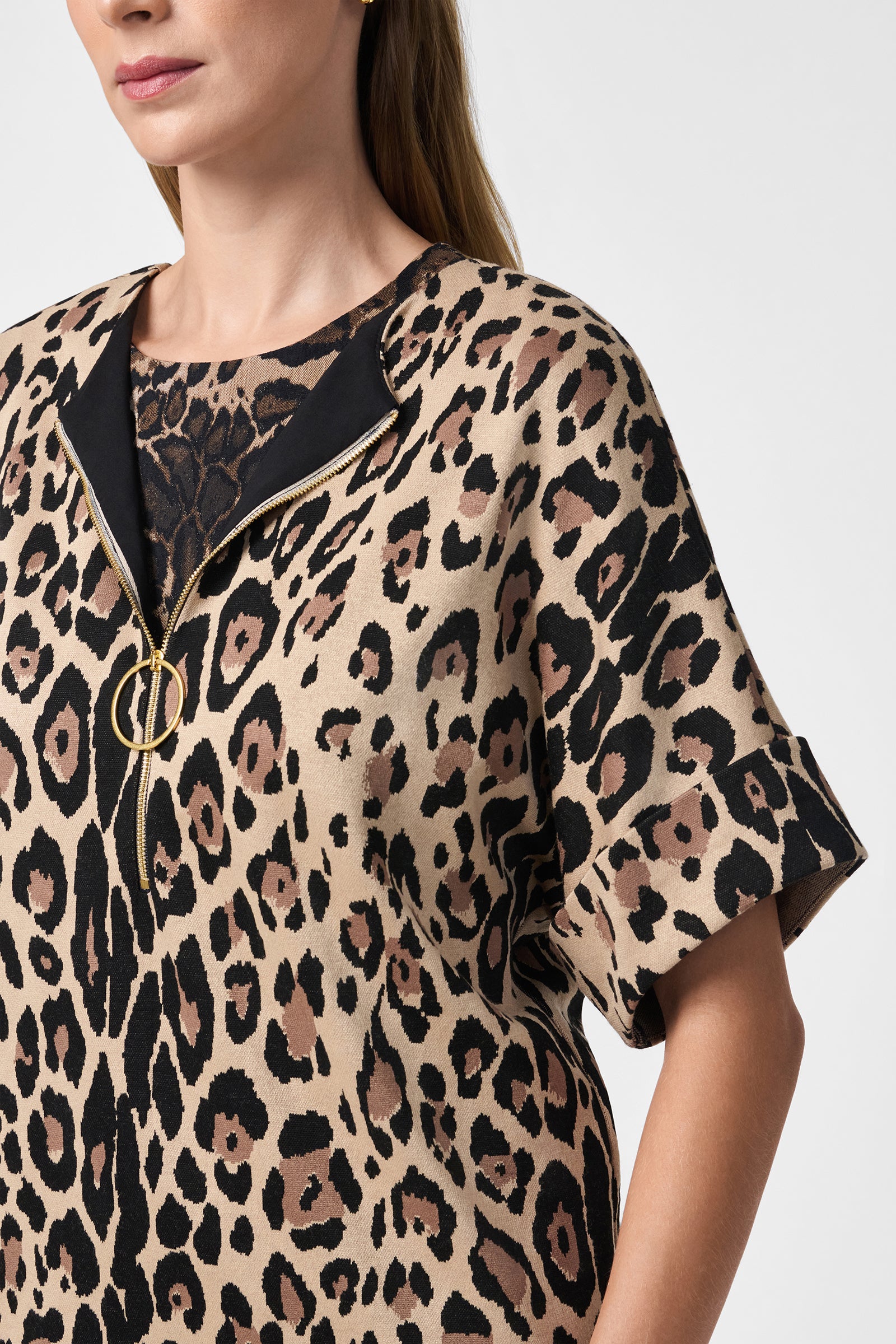 A woman wears the Stagehands Top—a short-sleeve, leopard print shirt with a black collar and gold zipper—over a black lace garment. She is shown from the shoulders up with straight blonde hair.