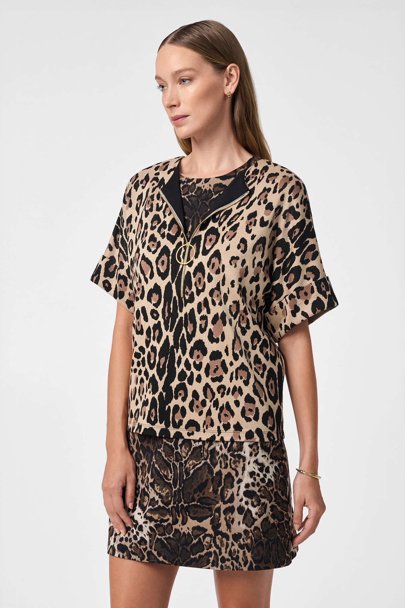 A woman with straight, long blonde hair models the Stagehands Top, a short-sleeved leopard-print shirt paired with a matching bold animal print skirt. She poses against a plain white background, gazing slightly to the side.