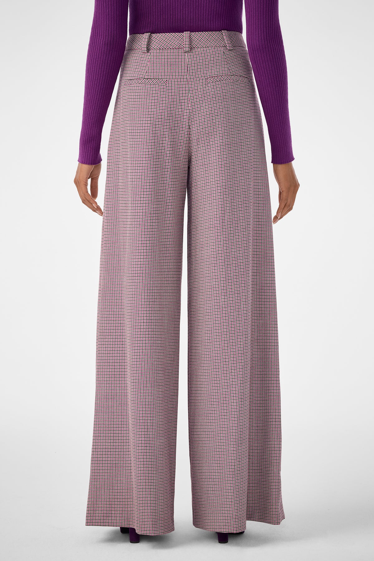 A person wearing the Solani Pant, featuring wide-leg, high-waisted plaid design, paired with a long-sleeved purple ribbed top and shown from the back against a plain light background.