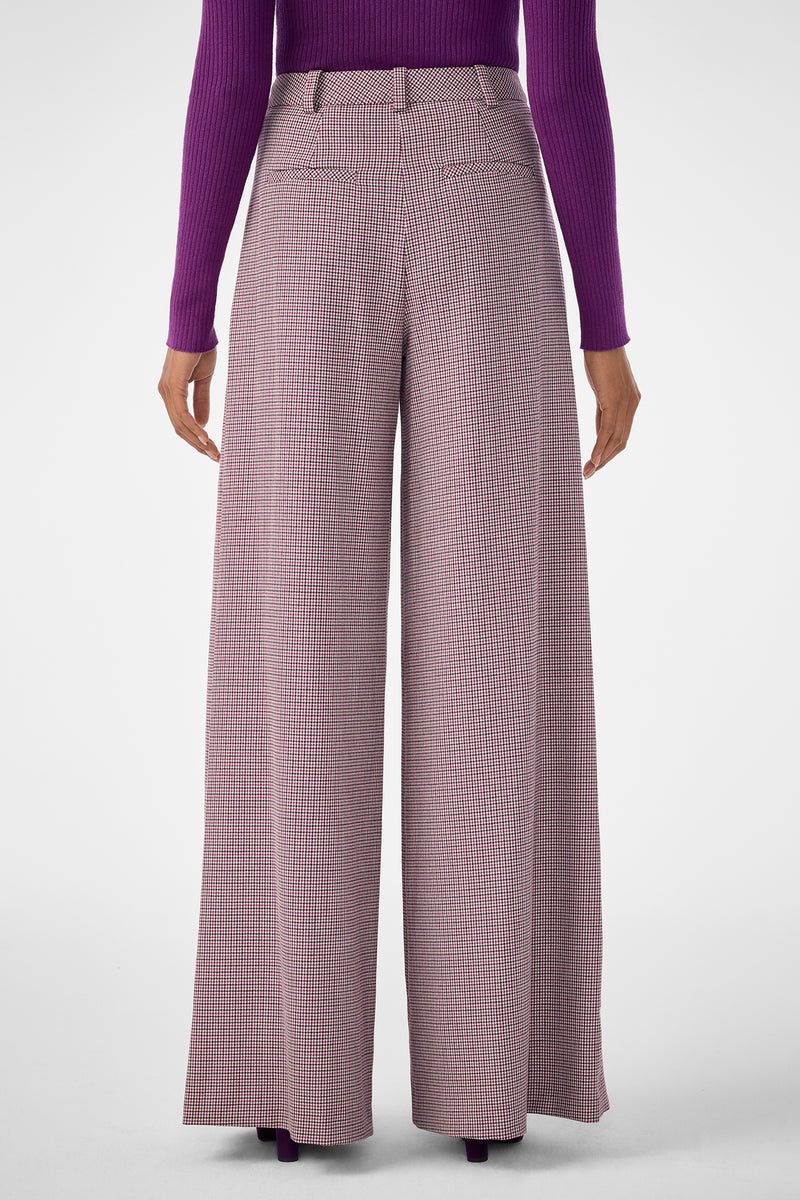 A person wearing the Solani Pant, featuring wide-leg, high-waisted plaid design, paired with a long-sleeved purple ribbed top and shown from the back against a plain light background.