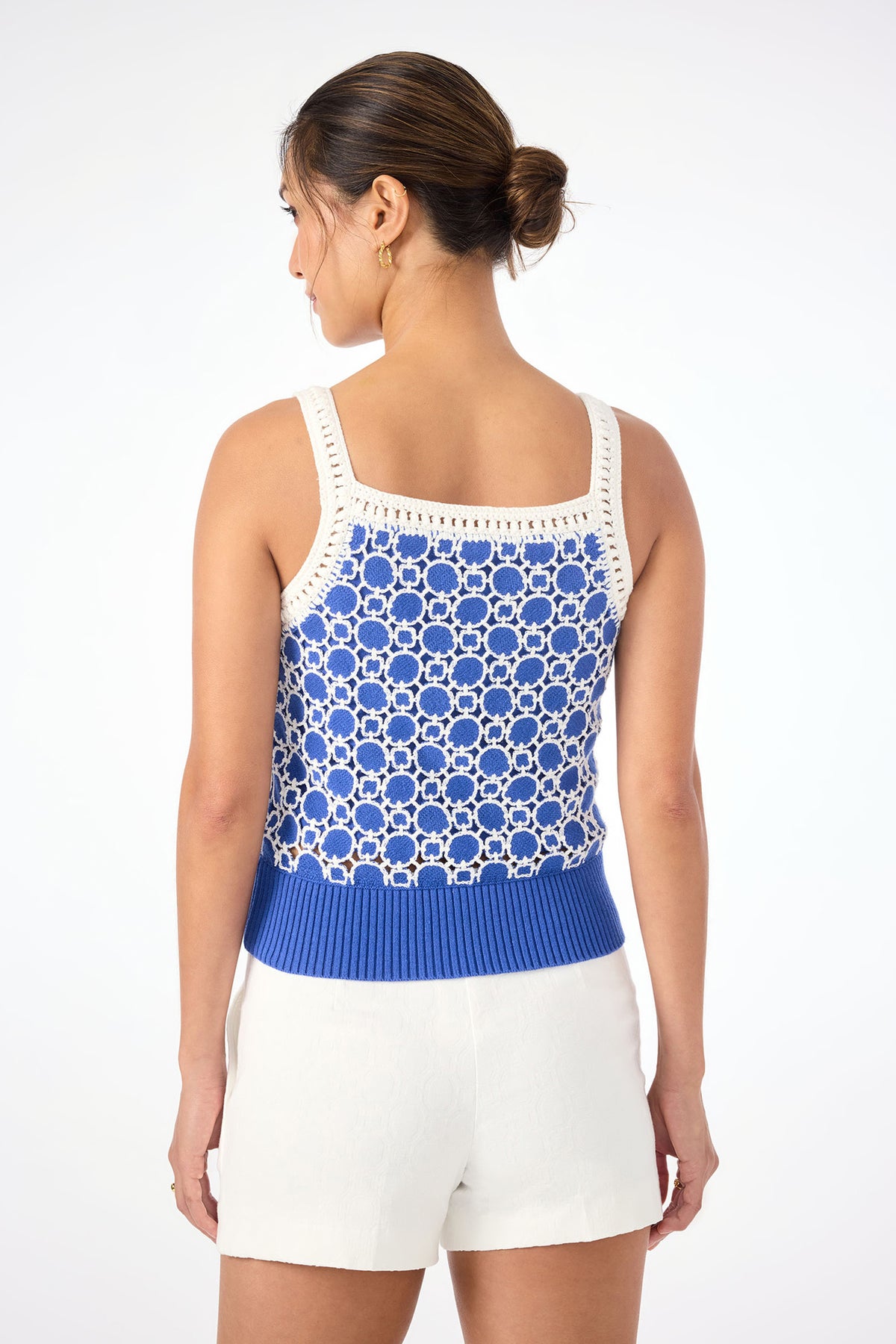 A woman with her hair in a low bun is seen from the back, wearing the Suez Straight Neck Knit Cami in blue and white paired with white shorts, set against a plain white background.