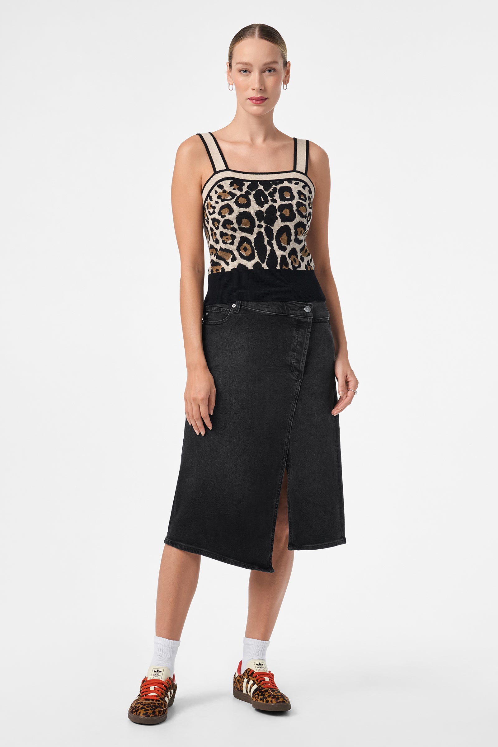 A woman stands facing forward, wearing the Casady Cami, a black wrap-style midi skirt, white socks, and animal print sneakers with red laces. Her hair is pulled back; she poses against a plain white background.