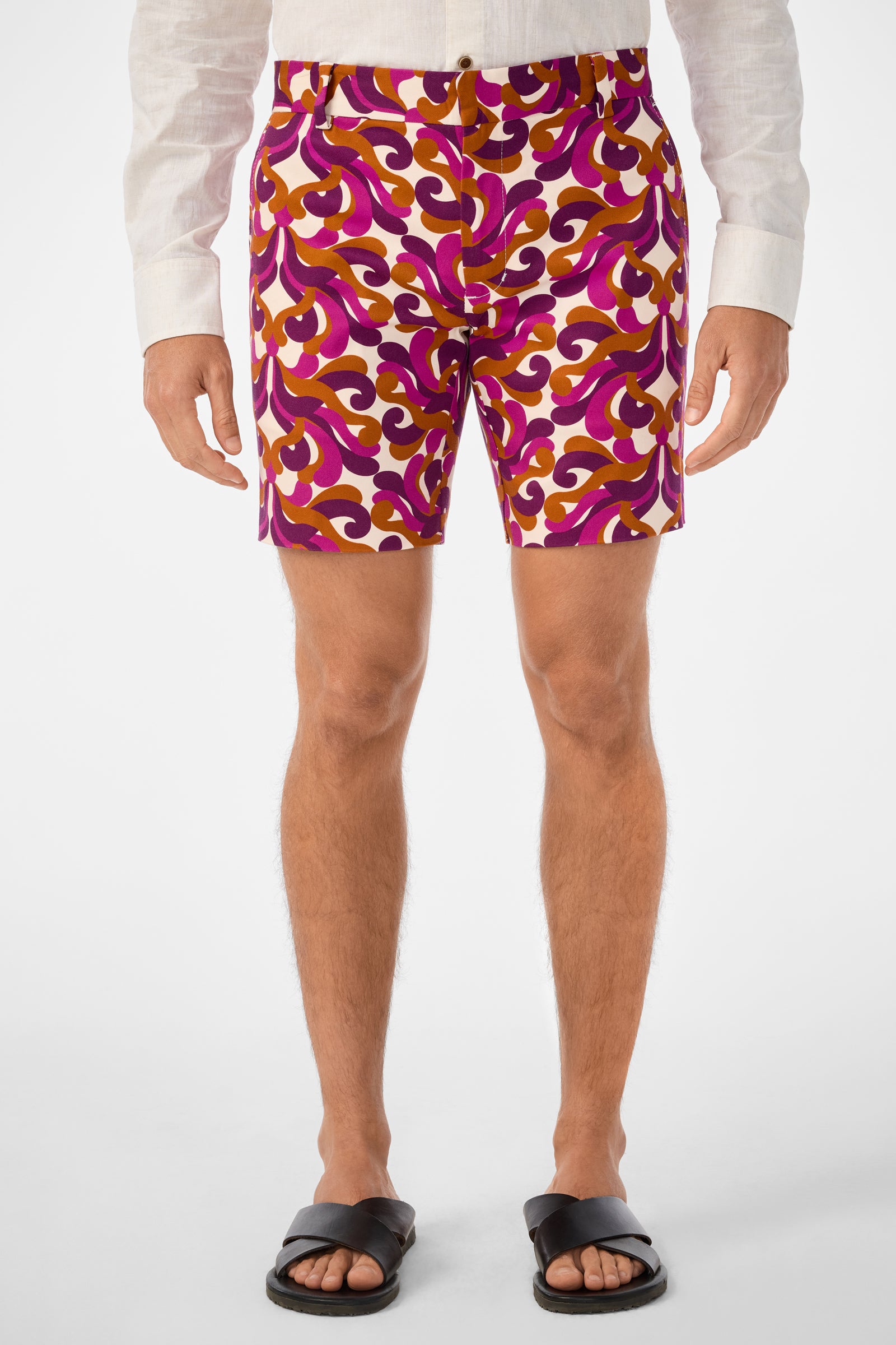 A person wearing a white long-sleeve shirt, Lawrence Short featuring colorful patterns in purple, orange, and white, and black sandals stands against a plain white background.