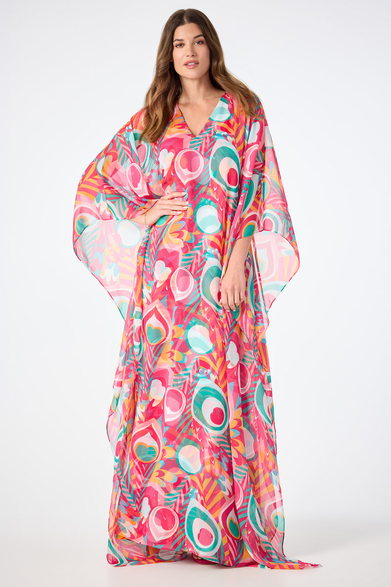 A woman wears the Salon Maxi Caftan Dress in Dramont, featuring vibrant abstract patterns, as she stands against a plain white background.