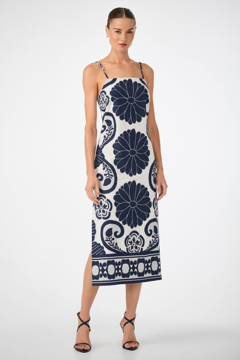 Woman wears the Marita 3 Sleeveless Dress in Fuyuko Fil Coupe—white midi with bold navy blue floral and geometric patterns—paired with black strappy heels, standing against a plain white background.