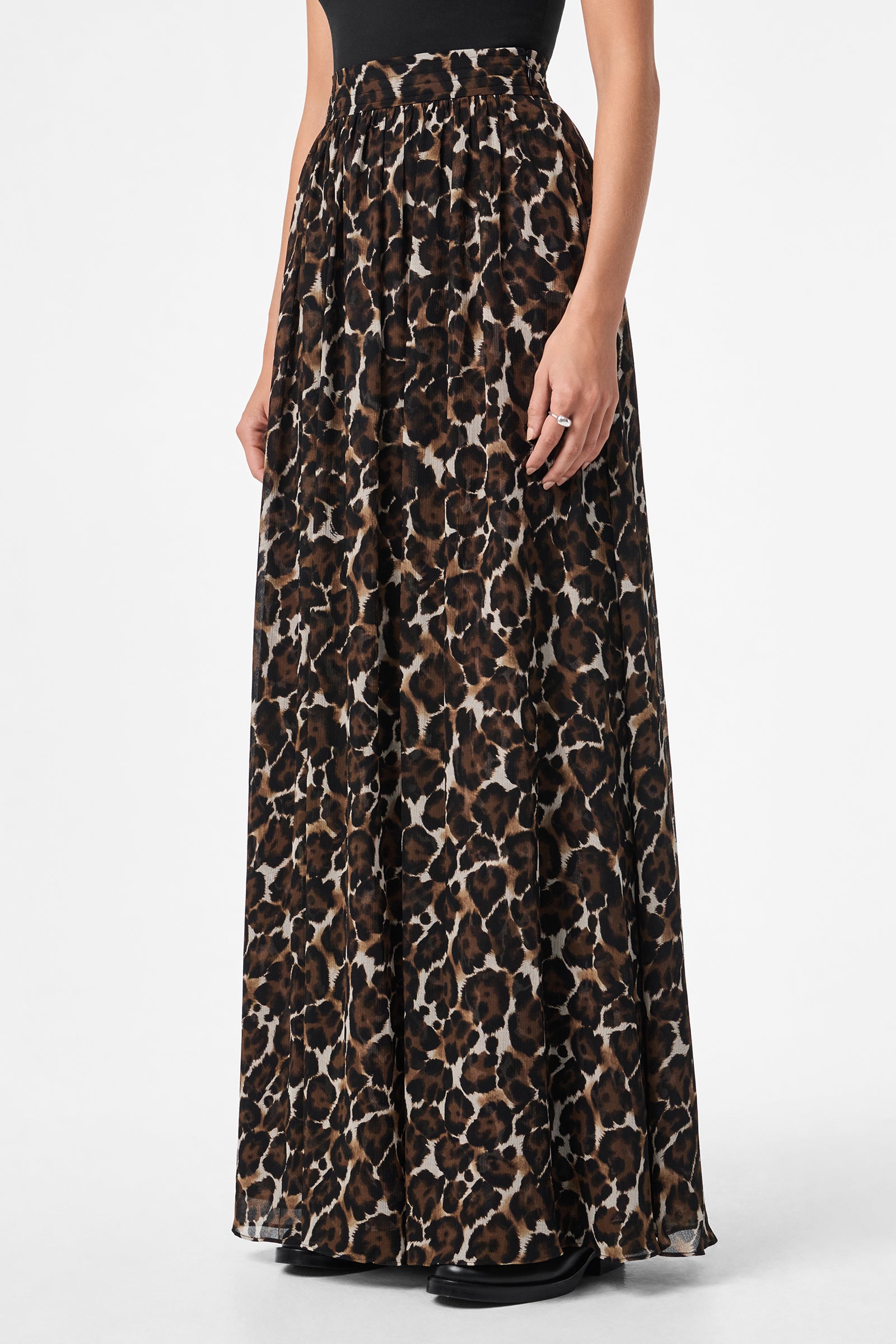 A person wearing the Bersha Skirt, a high-waisted, floor-length leopard print skirt with a loose, flowing fit, paired with a black top. Their arms are relaxed at their sides.