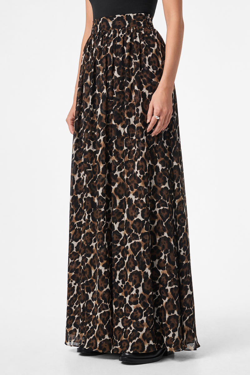 A person wearing the Bersha Skirt, a high-waisted, floor-length leopard print skirt with a loose, flowing fit, paired with a black top. Their arms are relaxed at their sides.