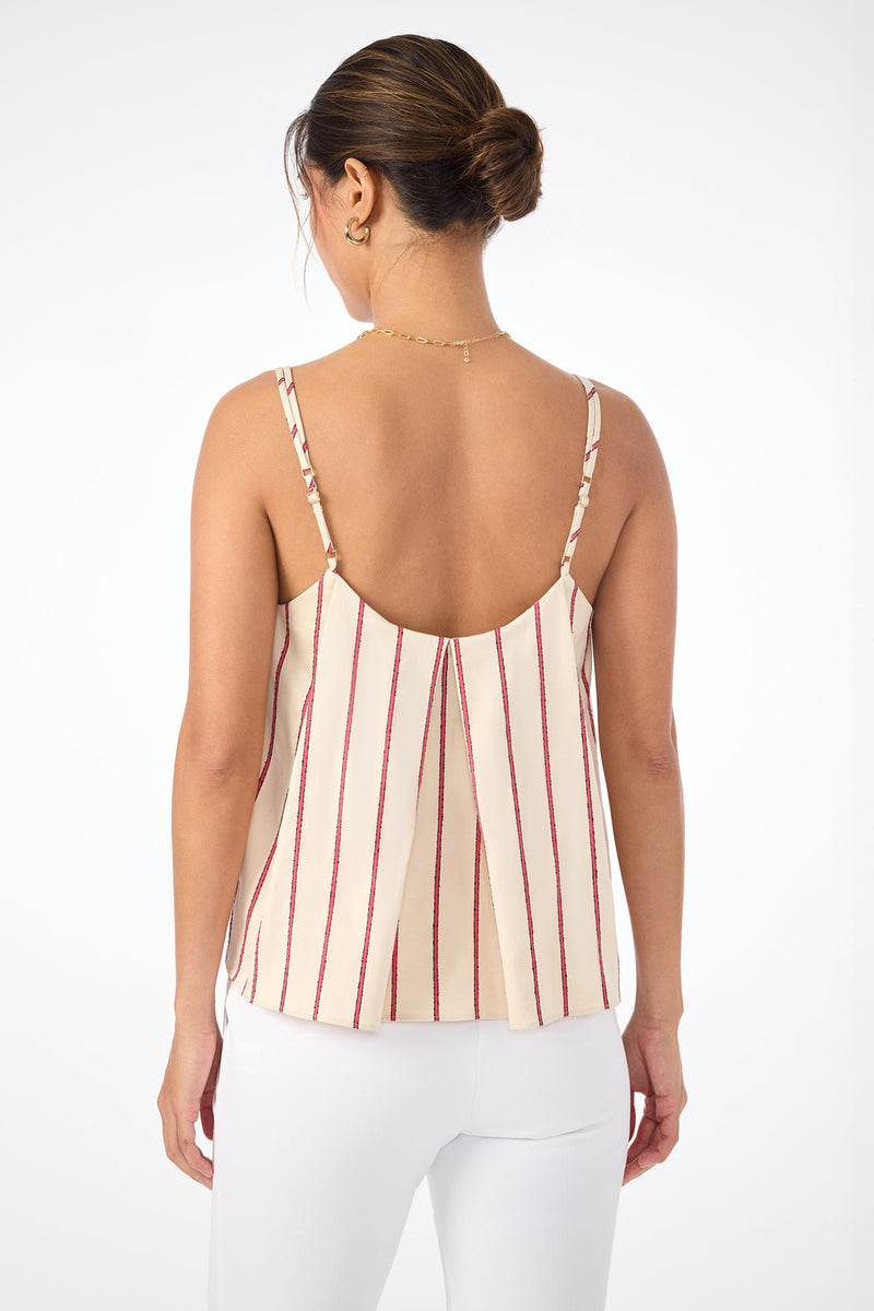 A woman with dark hair in a bun, wearing the Trouve Sleeveless A-Line Top in Solaire Stripe and white pants, stands with her back to the camera against a plain white background.