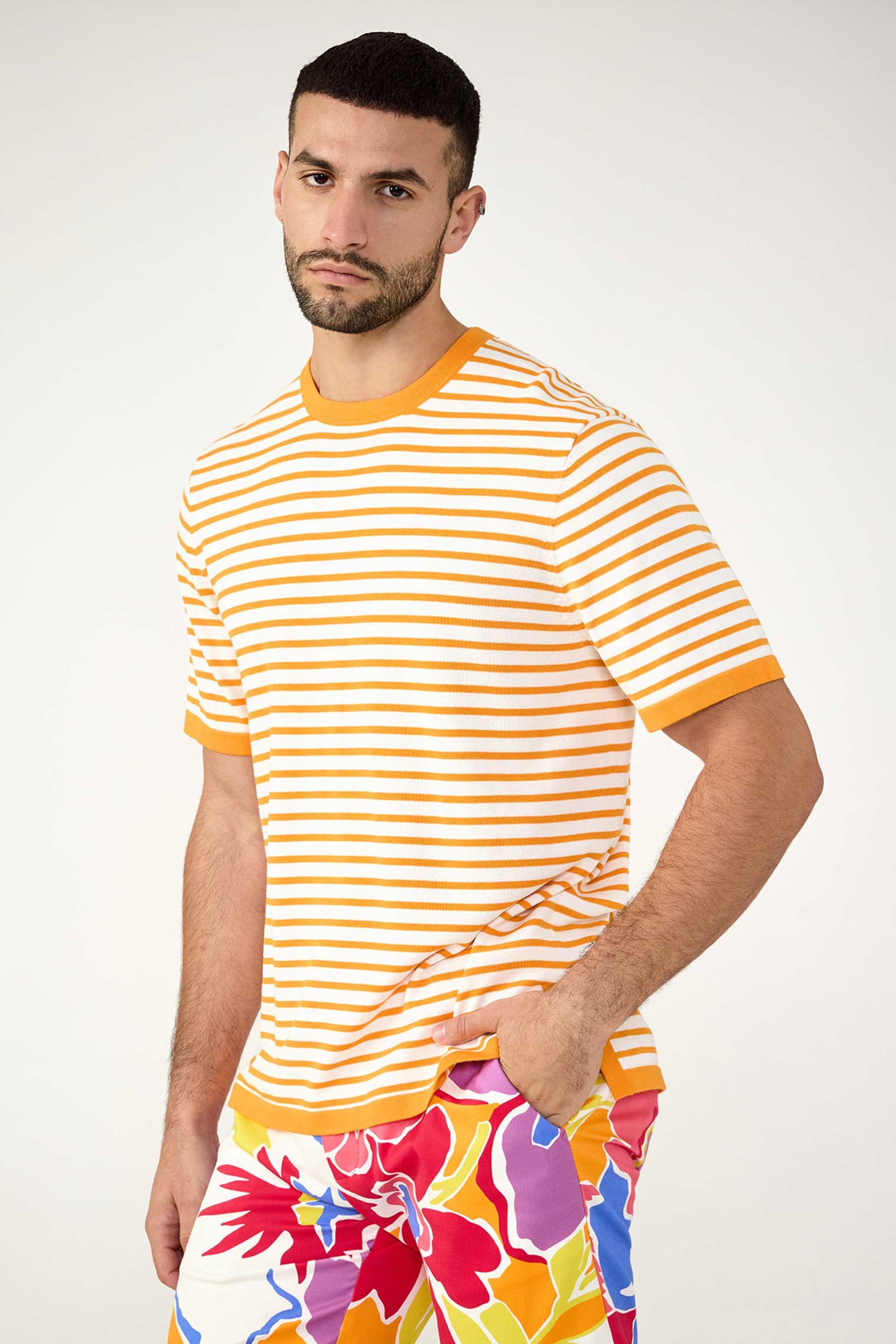 A man with short dark hair and a trimmed beard wears the Giovanni Stripe Short-Sleeve Pullover, an orange and white striped t-shirt, standing against a plain light background with a neutral expression.