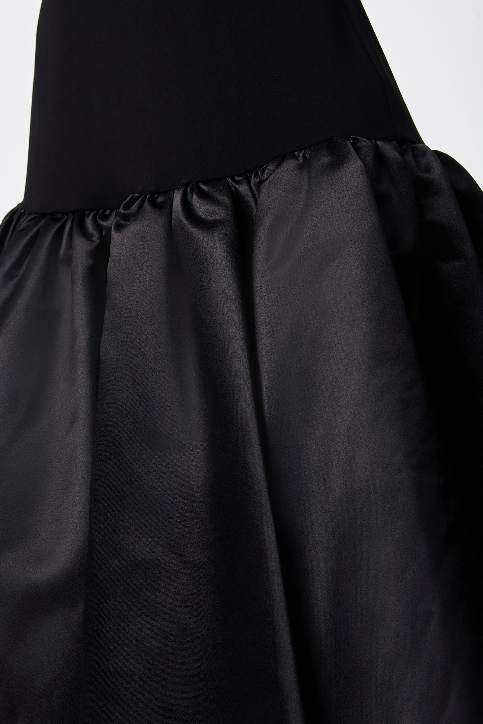 Close-up of the SINA DRESS - BLACK, showcasing its fitted bodice and gathered shiny satin skirt, emphasizing the fabric's texture and details.