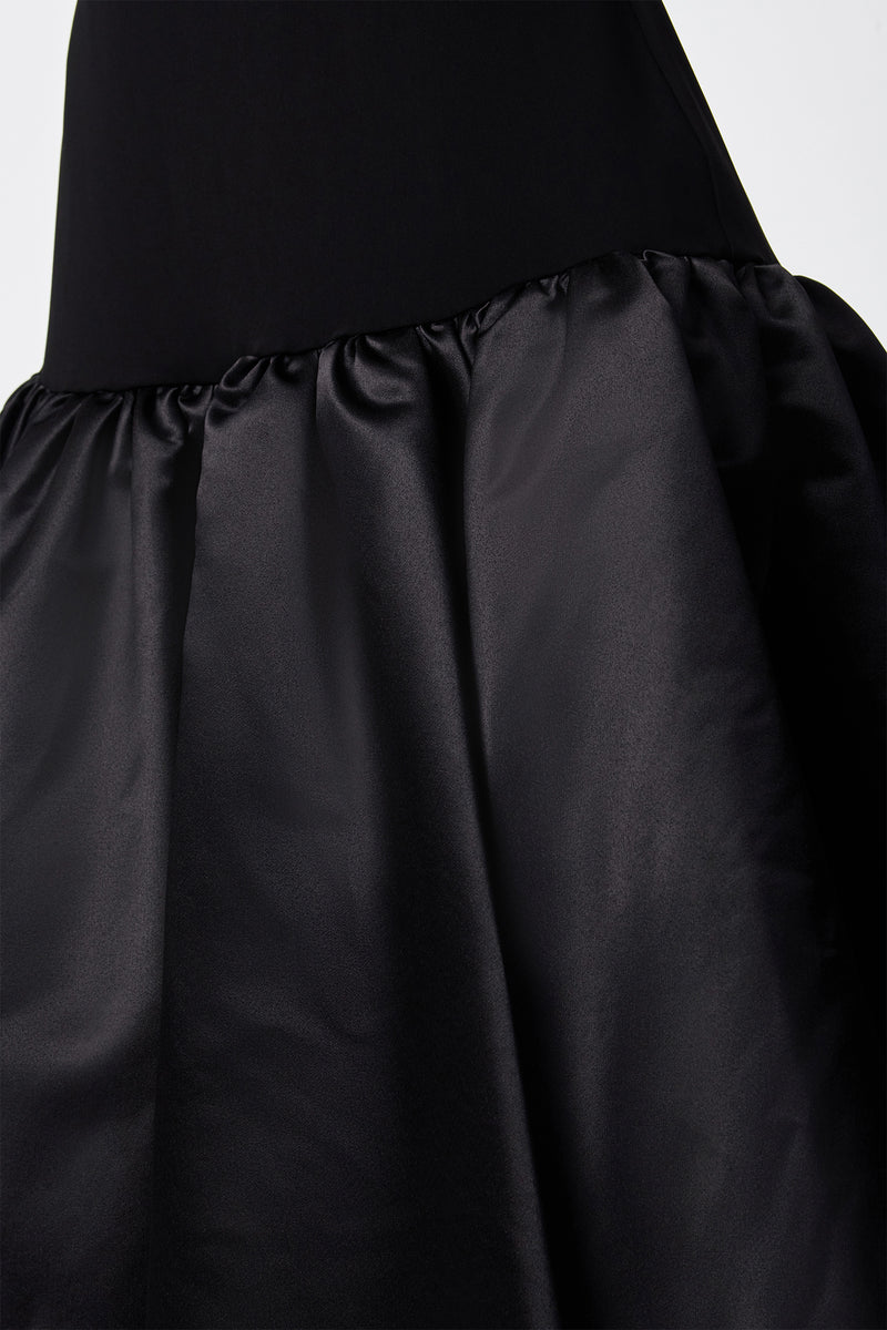Close-up of the SINA DRESS - BLACK, showcasing its fitted bodice and gathered shiny satin skirt, emphasizing the fabric's texture and details.