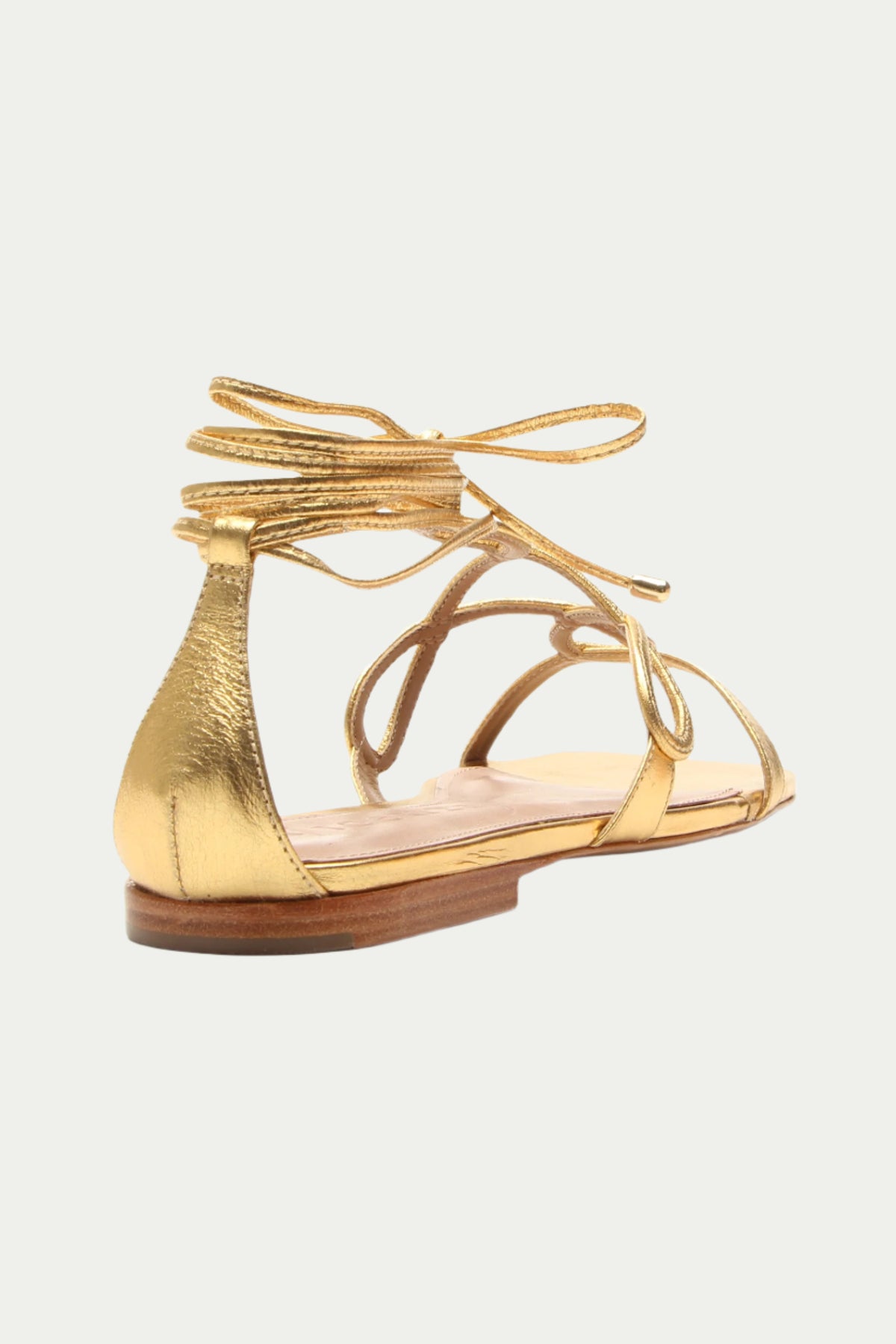 The Gana Strappy Leather Sandal in gold features thin straps and ankle ties, displayed from the back and side against a plain white background.