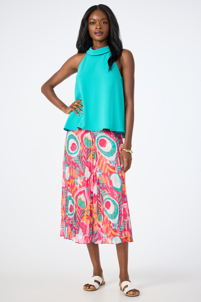 A woman stands against a white background wearing a sleeveless turquoise top and the Vitrolles Wide-Leg Crop Pants in Dramont, featuring vibrant pink, green, and orange patterns. She pairs them with white sandals and a gold bracelet.