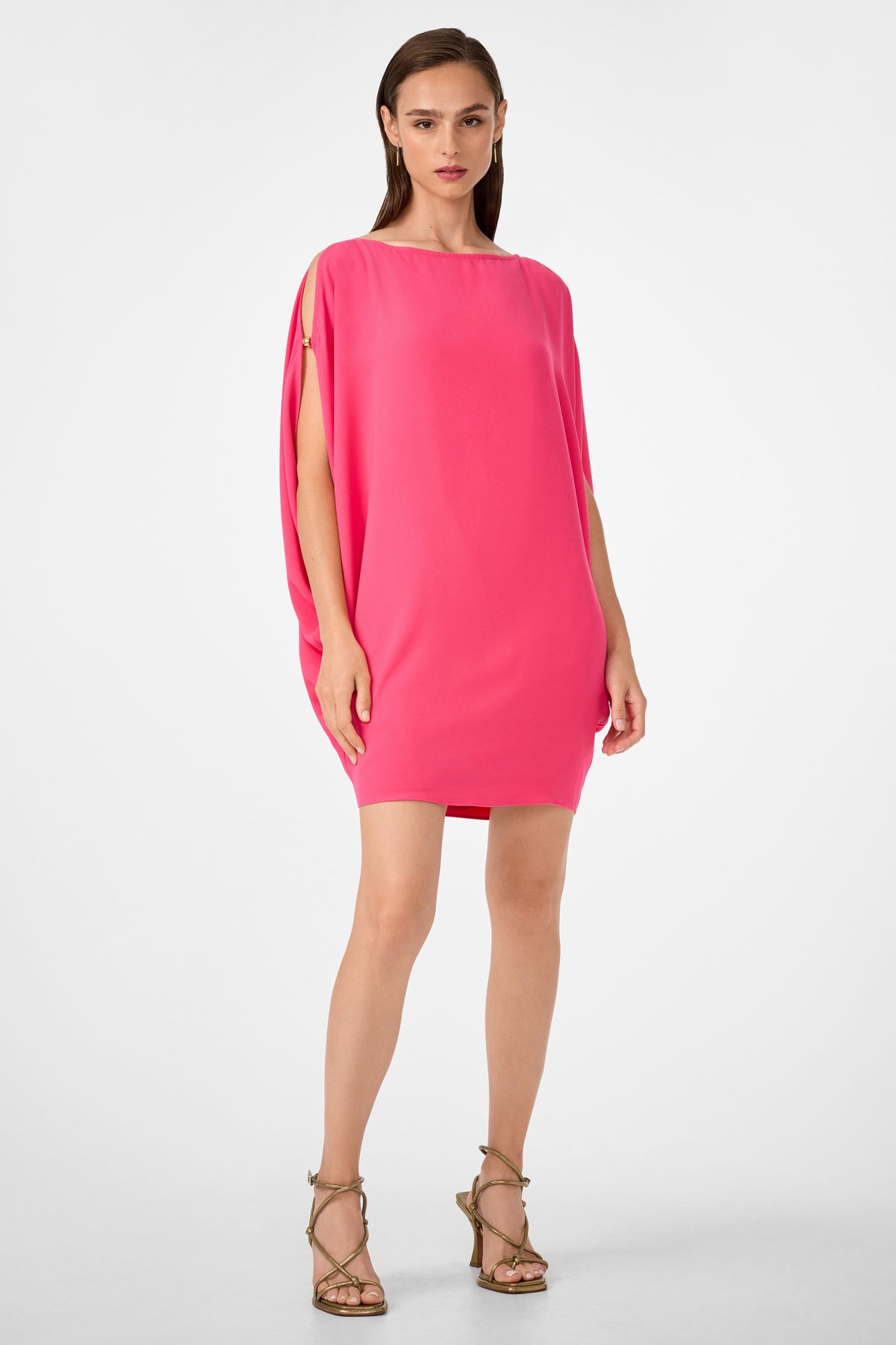 A woman with straight brown hair and a confident expression stands against a white background wearing the Razu Short Split Sleeve Mini Dress in Rosewater and strappy high-heeled sandals.