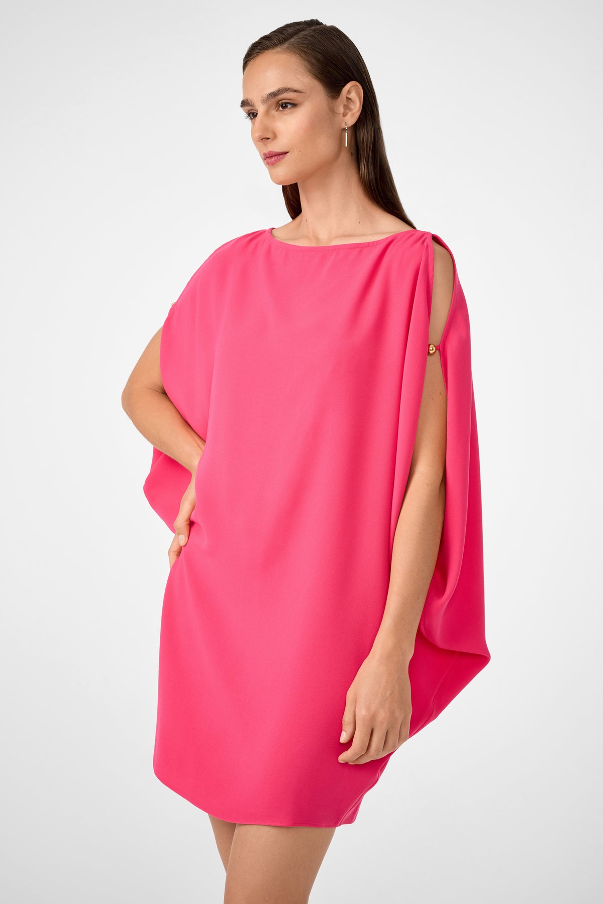 A woman poses against a plain light background wearing the Razu Short Split Sleeve Mini Dress in bright pink, which features a loose fit and open shoulder details; one hand is on her hip while the other hangs by her side.