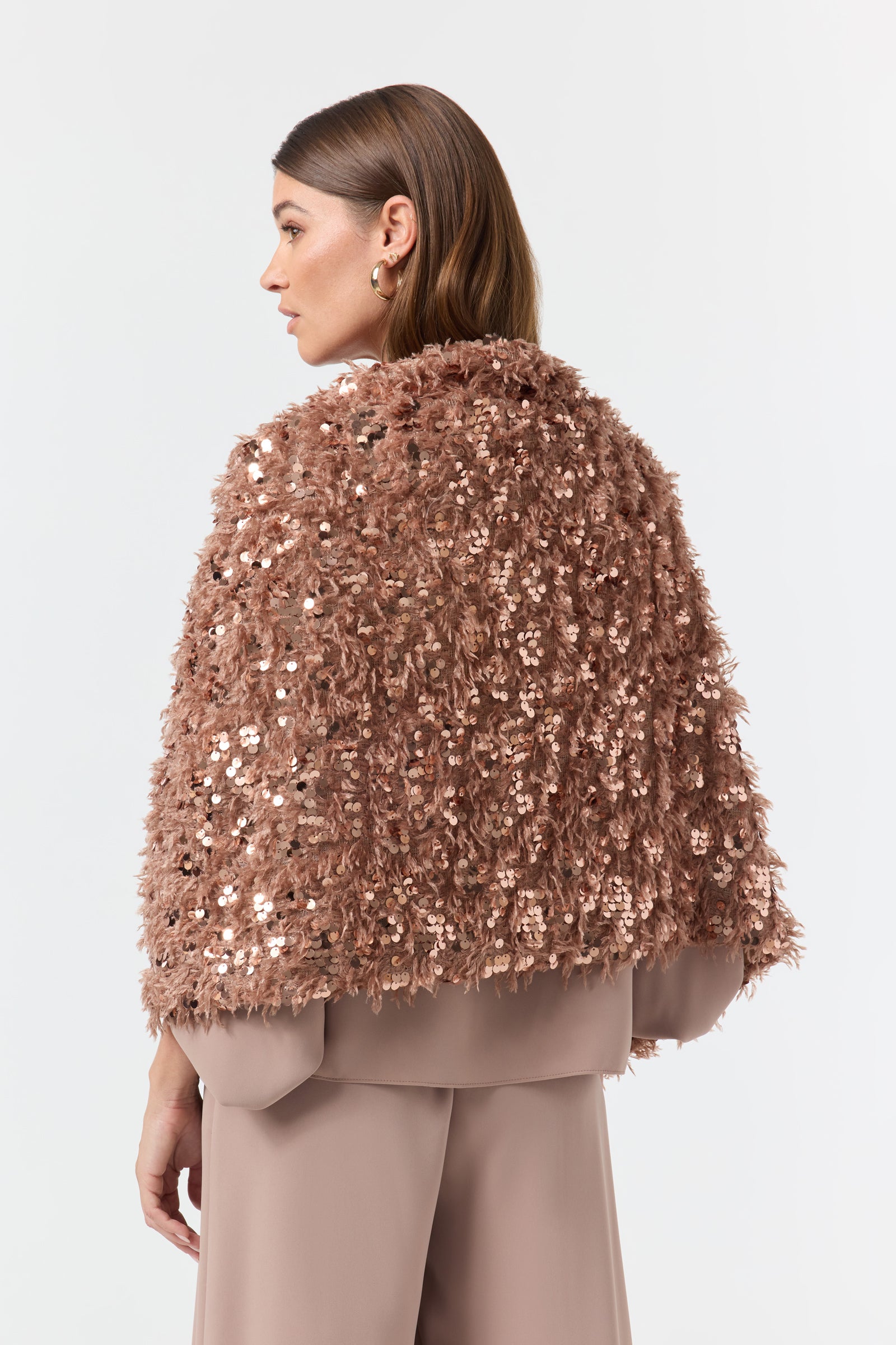A woman stands sideways in wide mauve pants and a textured, shiny Fete Faux Fur Stole. Her straight brown hair is tucked behind her ear, against a plain white background.