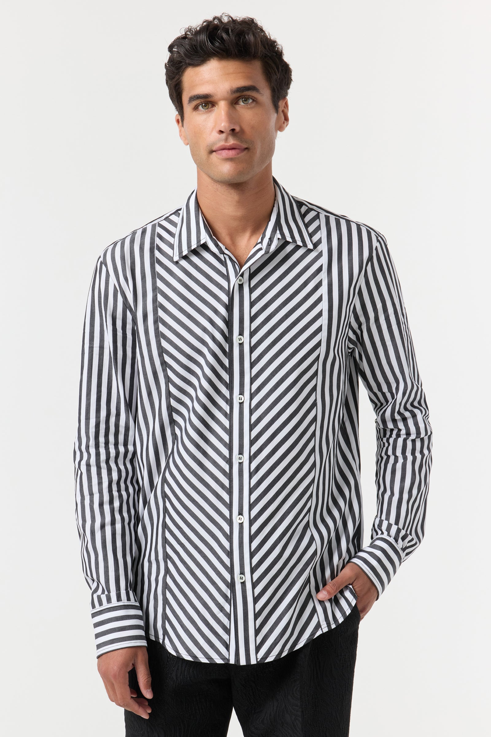 A man with short dark hair wears the Brody Tux Shirt, a long-sleeve button-up featuring bold black and white diagonal and vertical stripes. He stands against a plain white background with one hand in his pocket.