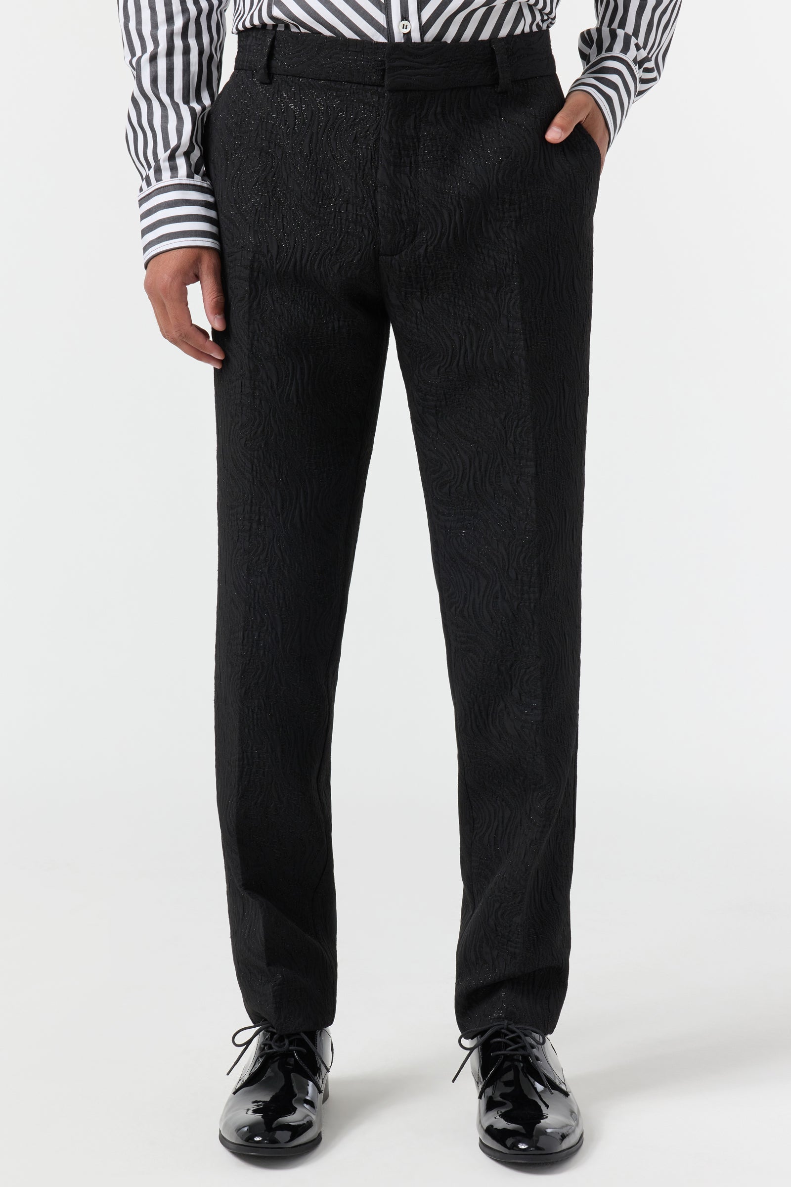 A person wearing the Clyde Slim Trouser - Metallic Groove, paired with a black and white striped shirt and shiny black dress shoes, stands against a plain white background. The image shows them cropped from the shoulders down.