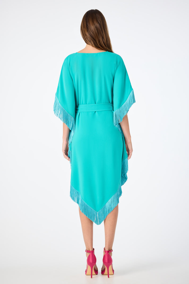 A woman stands with her back to the camera, wearing the Toulouse Short-Sleeve Fringe Dress in turquoise and bright pink high-heeled shoes, set against a plain white background.