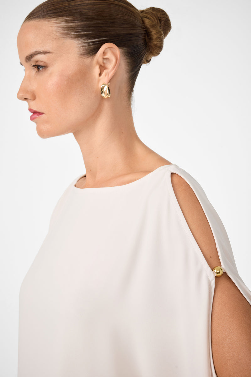 A woman with hair in a sleek bun wears gold hoop earrings and the off-white Razu Short Split Sleeve Mini Dress with shoulder cut-outs and gold buttons, shown in profile against a plain white background.