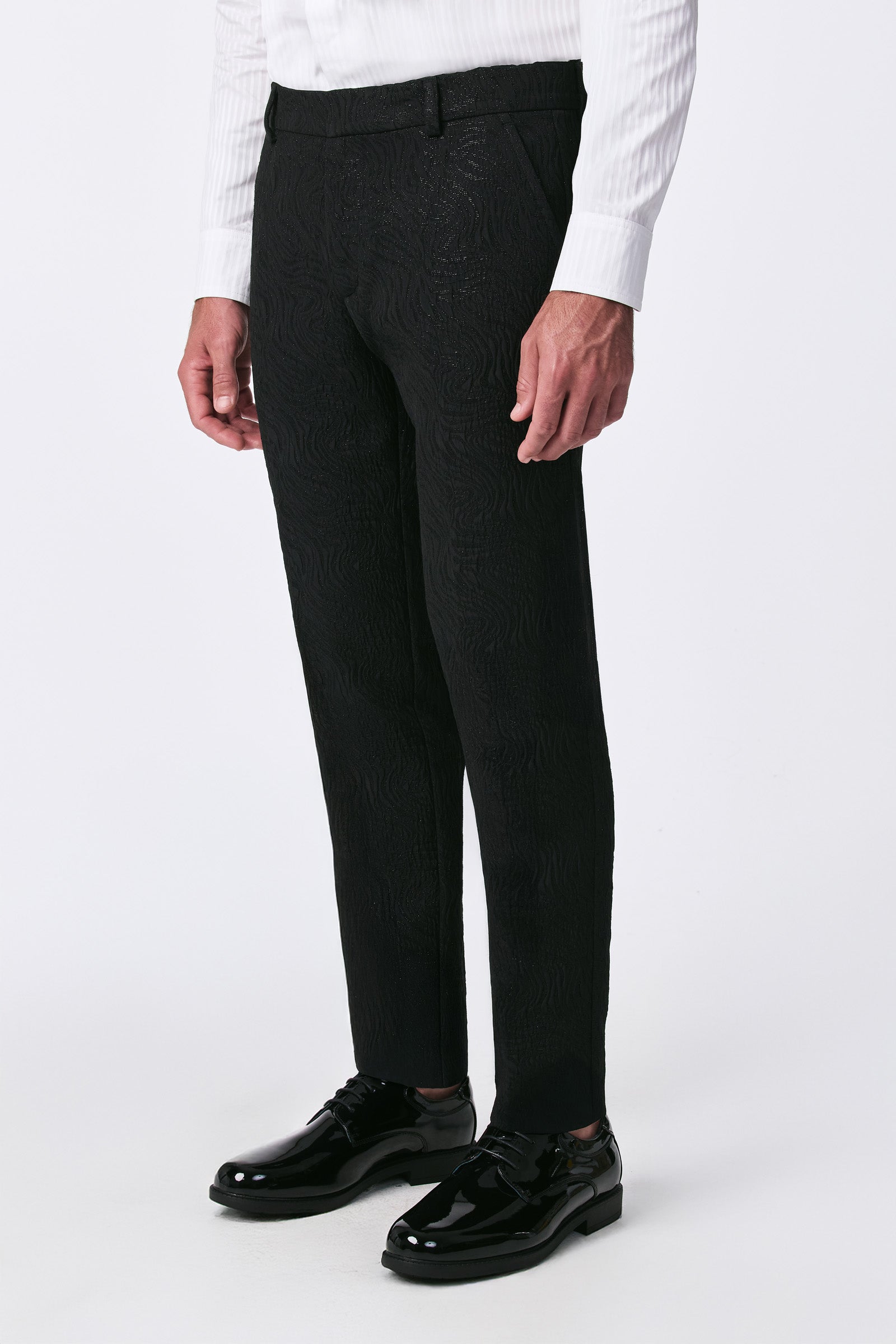 A person dressed in the Miles Blazer's textured black dress pants, paired with a white shirt and shiny black shoes, is shown from the waist down against a plain white background.
