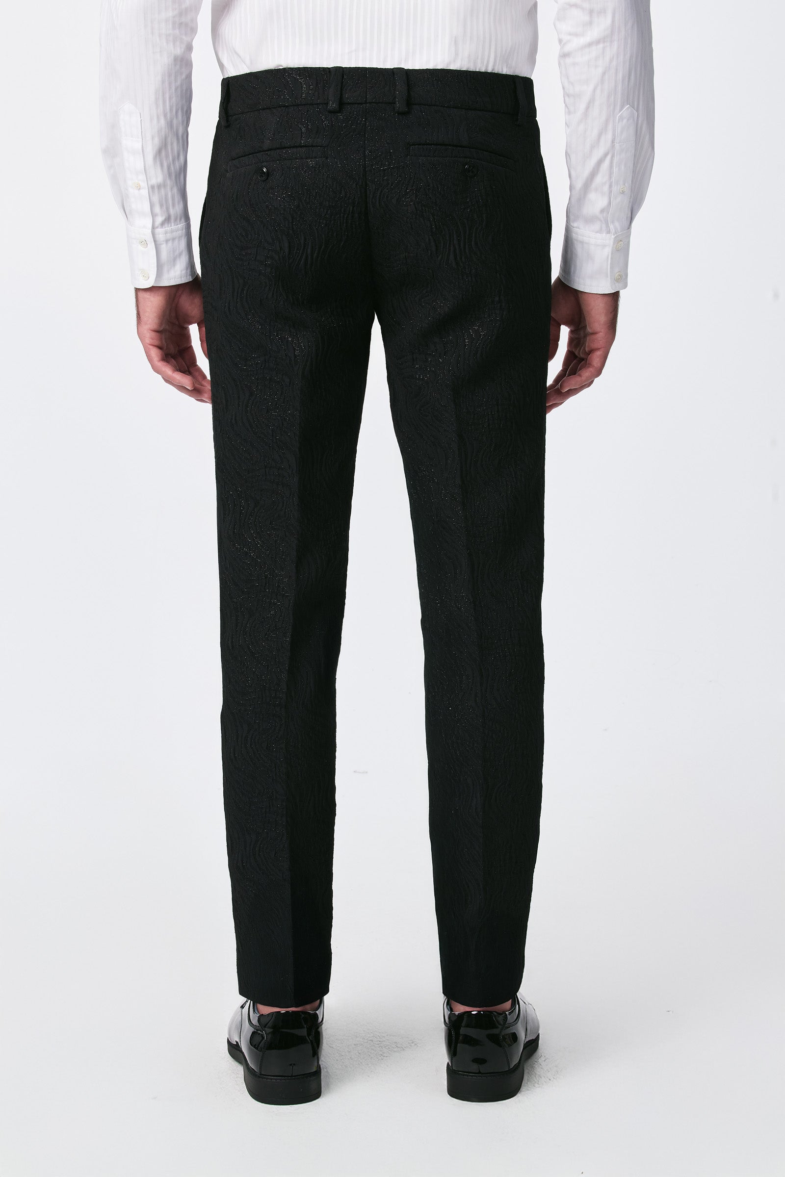 A man stands with his back to the camera against a plain white background, wearing the Miles Blazer with black textured dress pants, a white dress shirt, and shiny black dress shoes.