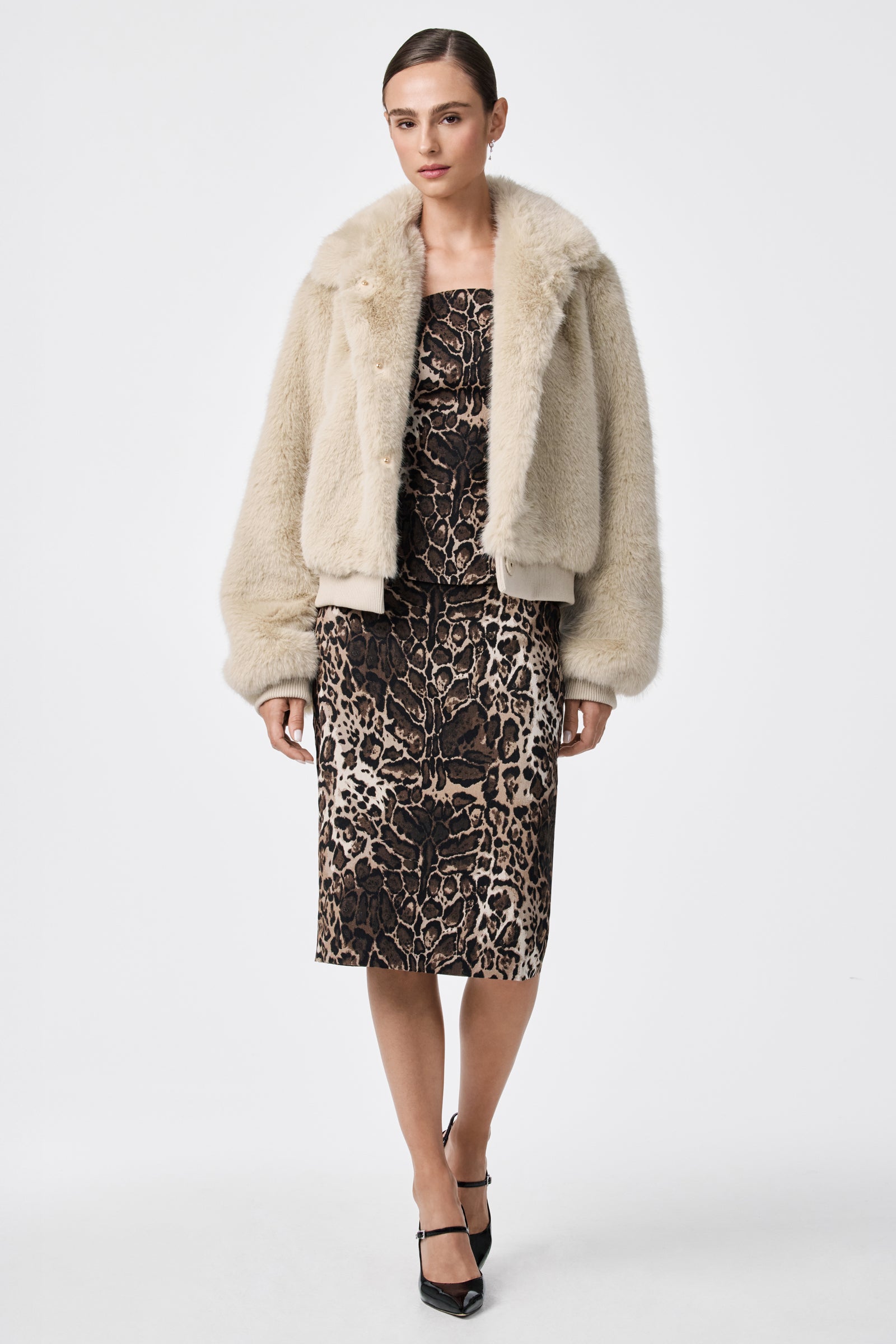 A woman stands against a white background wearing the Morris Short Faux Fur Coat over a fitted, knee-length leopard print dress and black pointed heels. Her hair is tied back, and she has a neutral expression.
