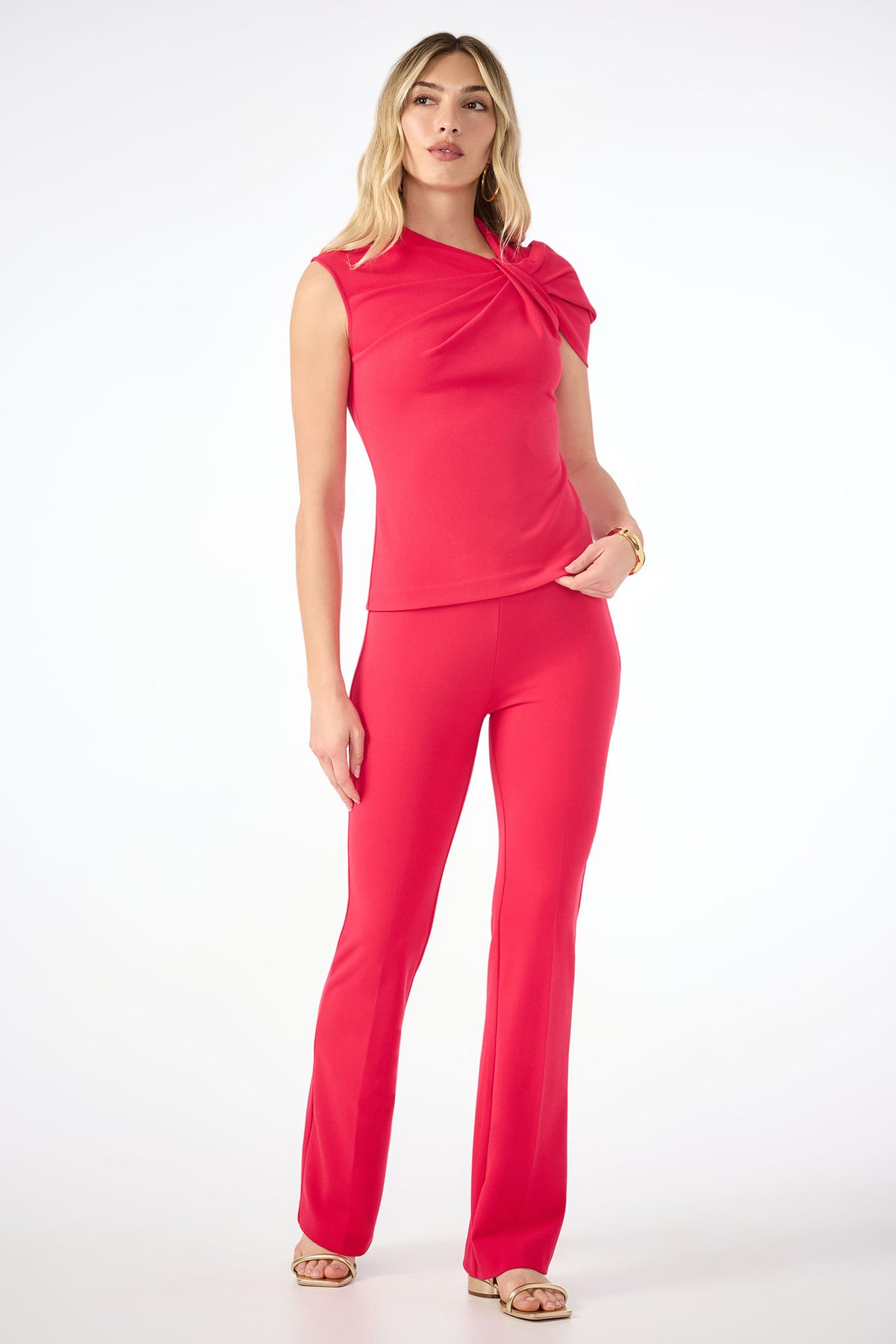 A woman with blonde hair, neutral makeup, and sandals poses against a white background wearing bright red Jacoba Slim-Fit Bootcut Pants and a matching sleeveless top with a knotted shoulder detail.