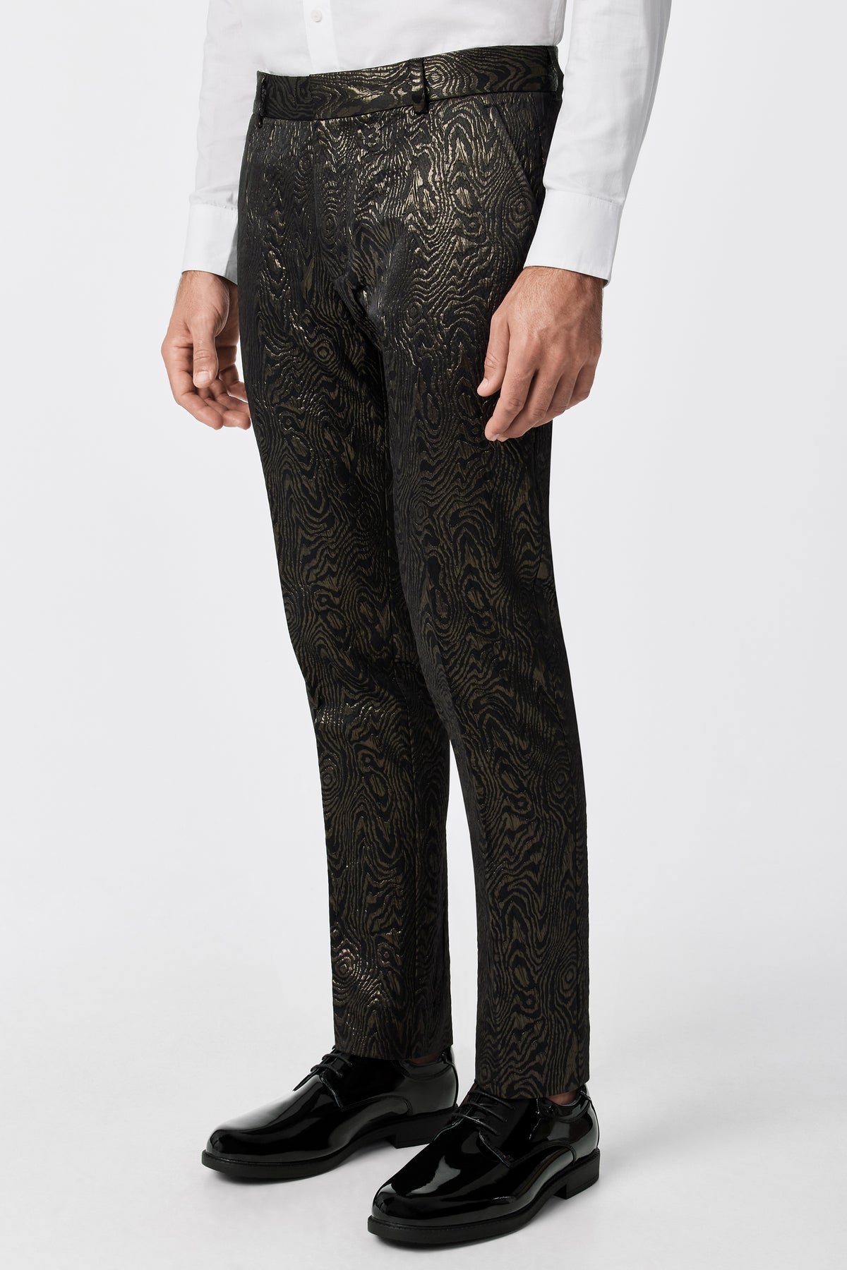 A person wearing the Clyde Slim Trouser - Fette Swirl with a white dress shirt and shiny black dress shoes, standing against a plain white background.
